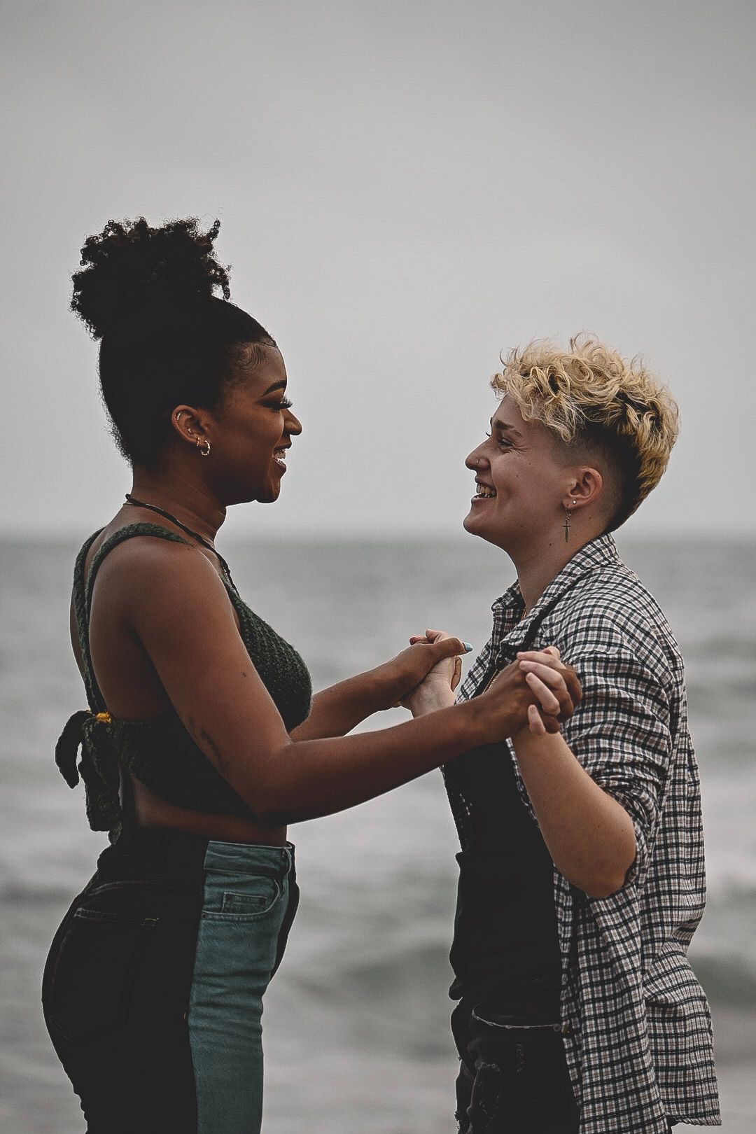 Two people share an intimate moment on a beach with a moody grey sky in the background.