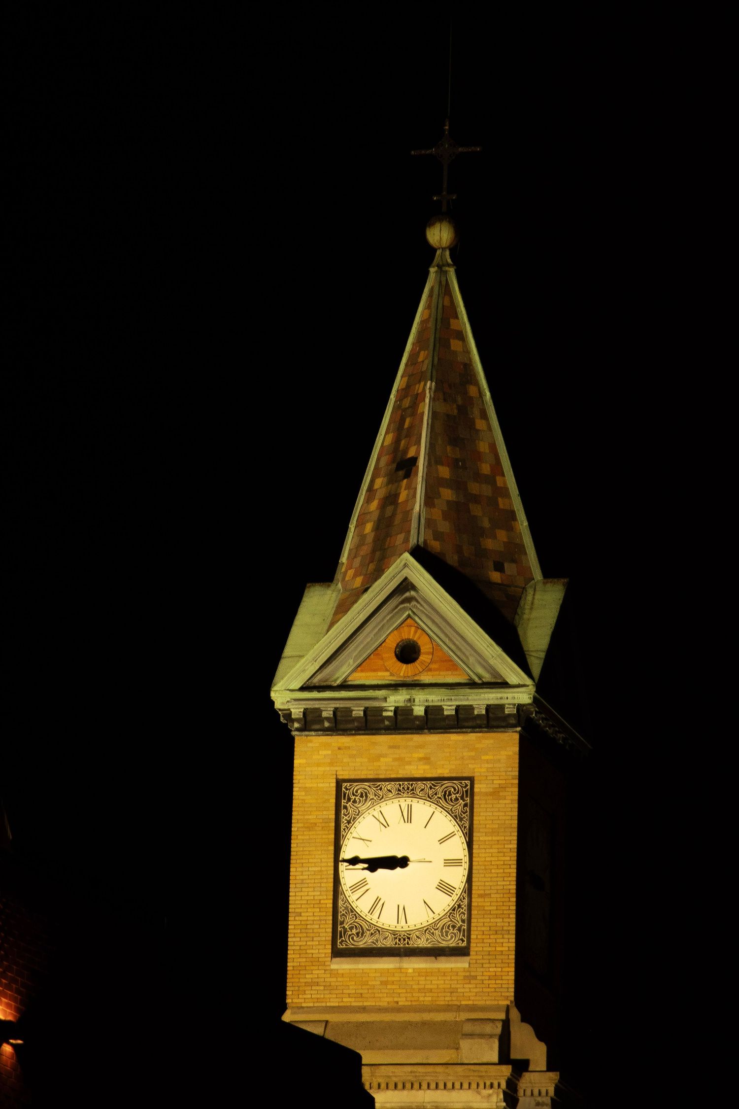 Illuminated church clock tower spire against dark night sky.