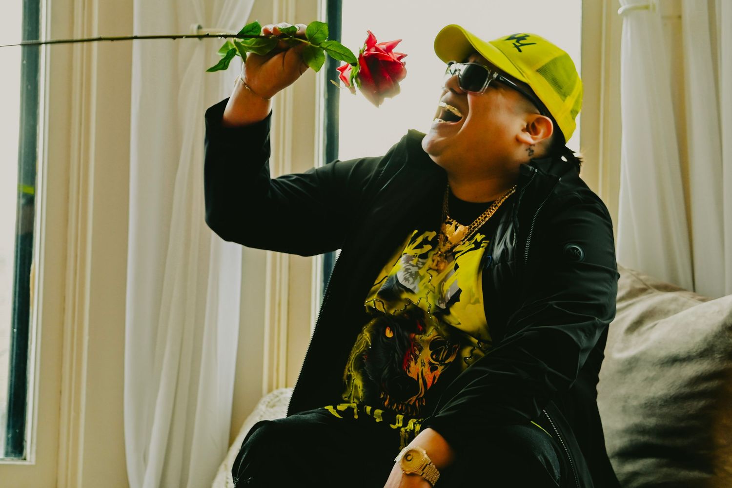 Person in yellow cap and black jacket holding up something while sitting on couch with floral decor.