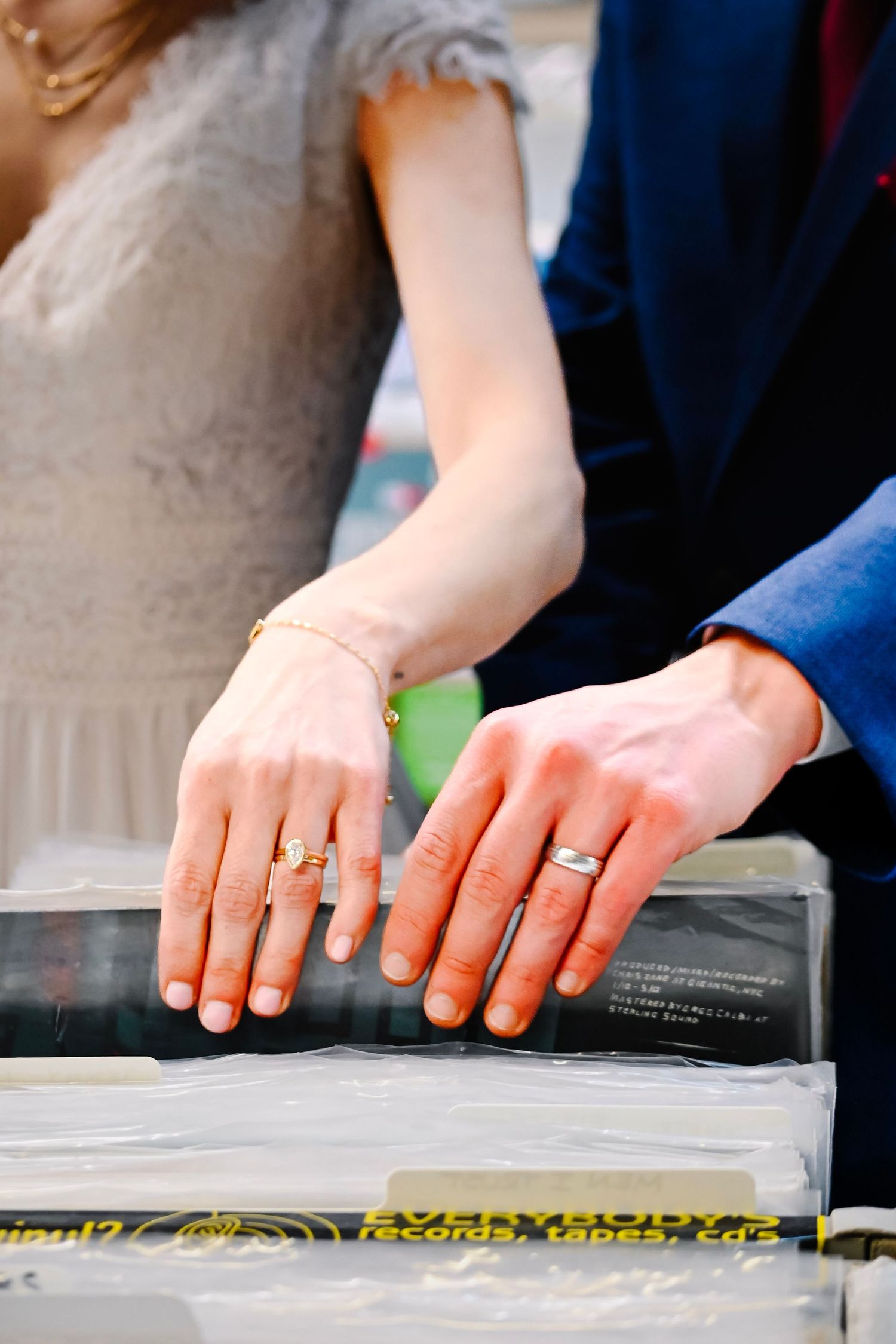 Newlywed couple placing hands on vinyl record, showing off wedding rings and gold bracelet.