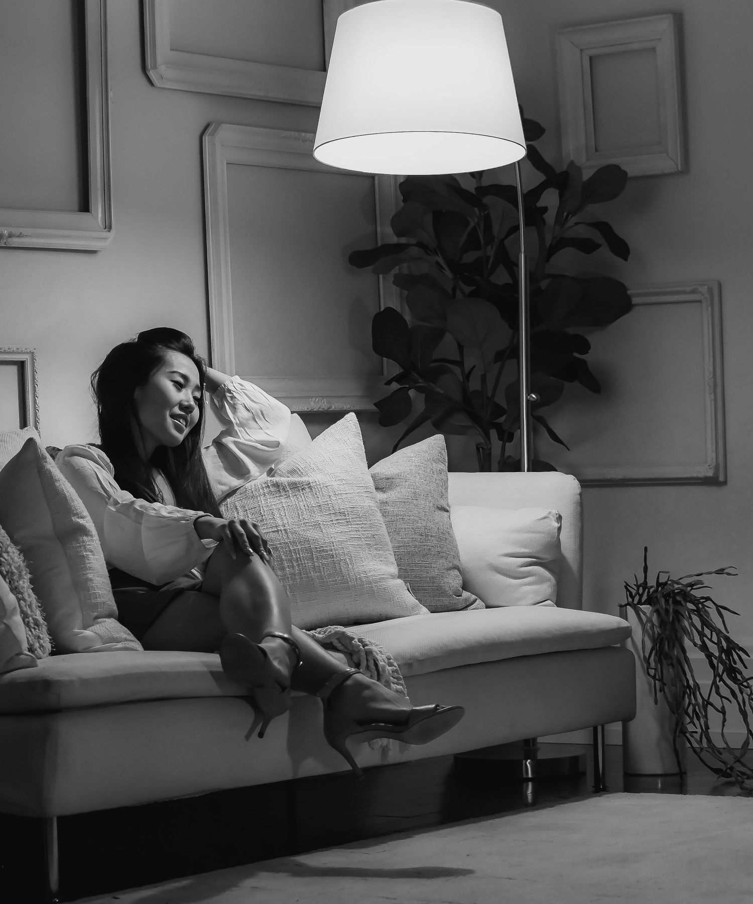 Black and white image of woman lounging on modern sofa beneath white lamp shade.