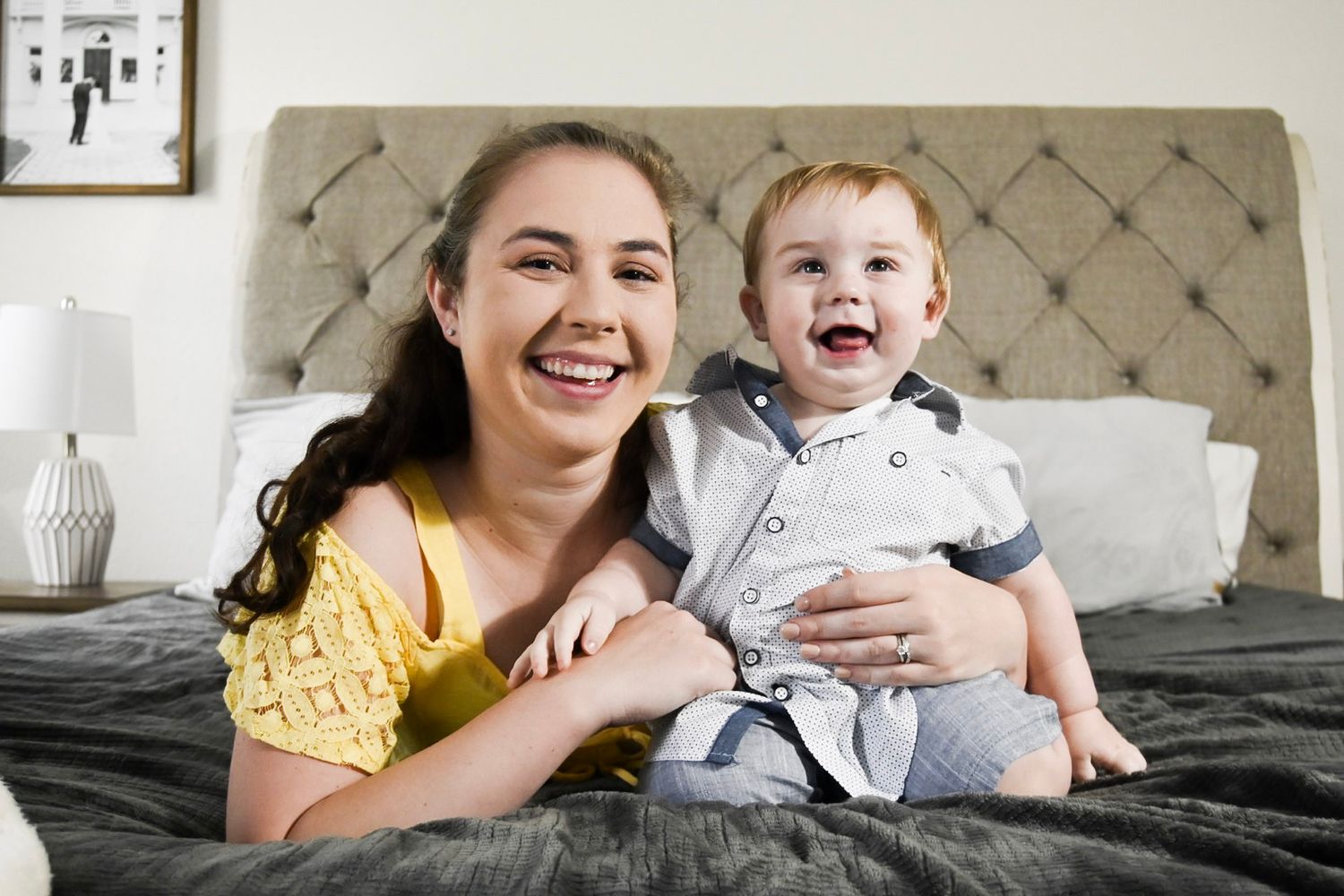 Joyful interactions between parent and child on grey bedding with decorative wall art.