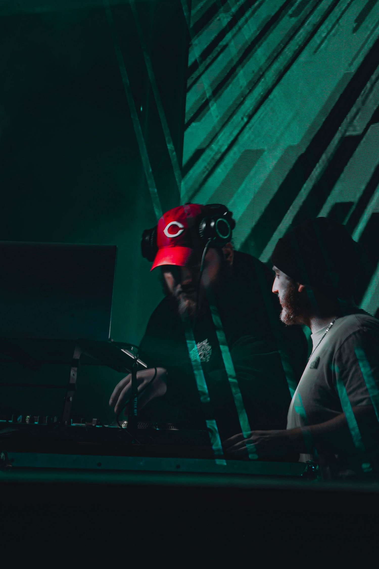 Two DJs performing at a dark venue with moody green lighting.