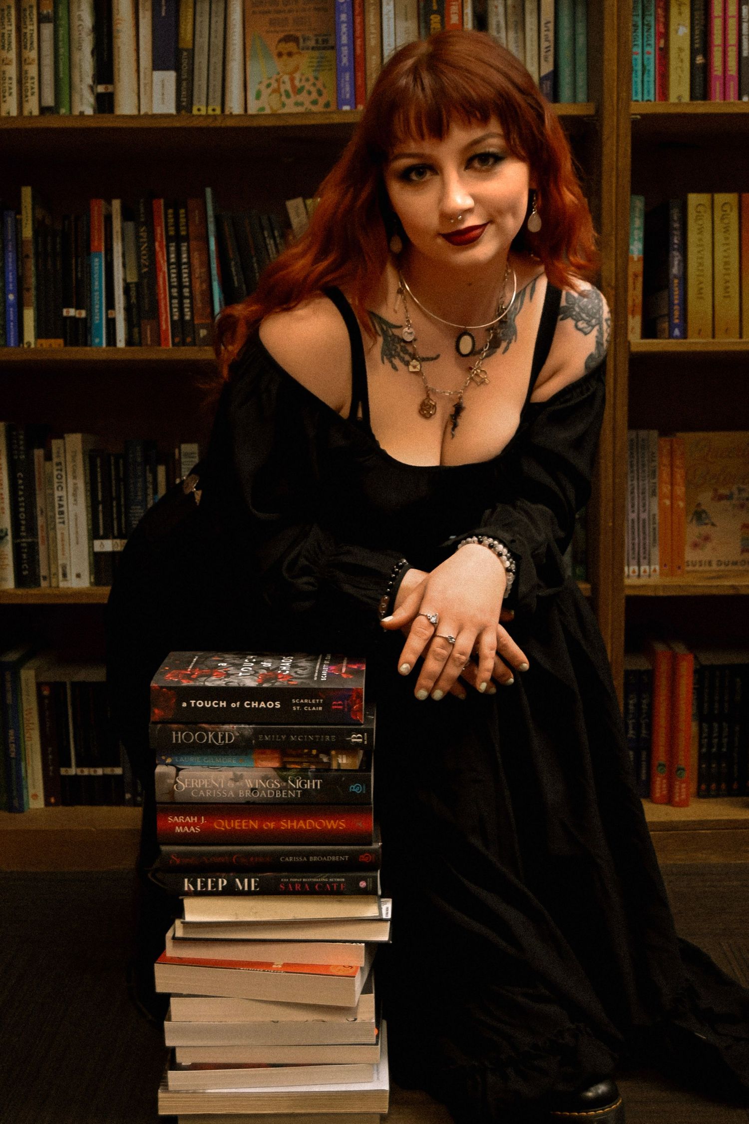 A person in gothic attire poses with a stack of books against a bookshelf backdrop in a series of connected photos.
