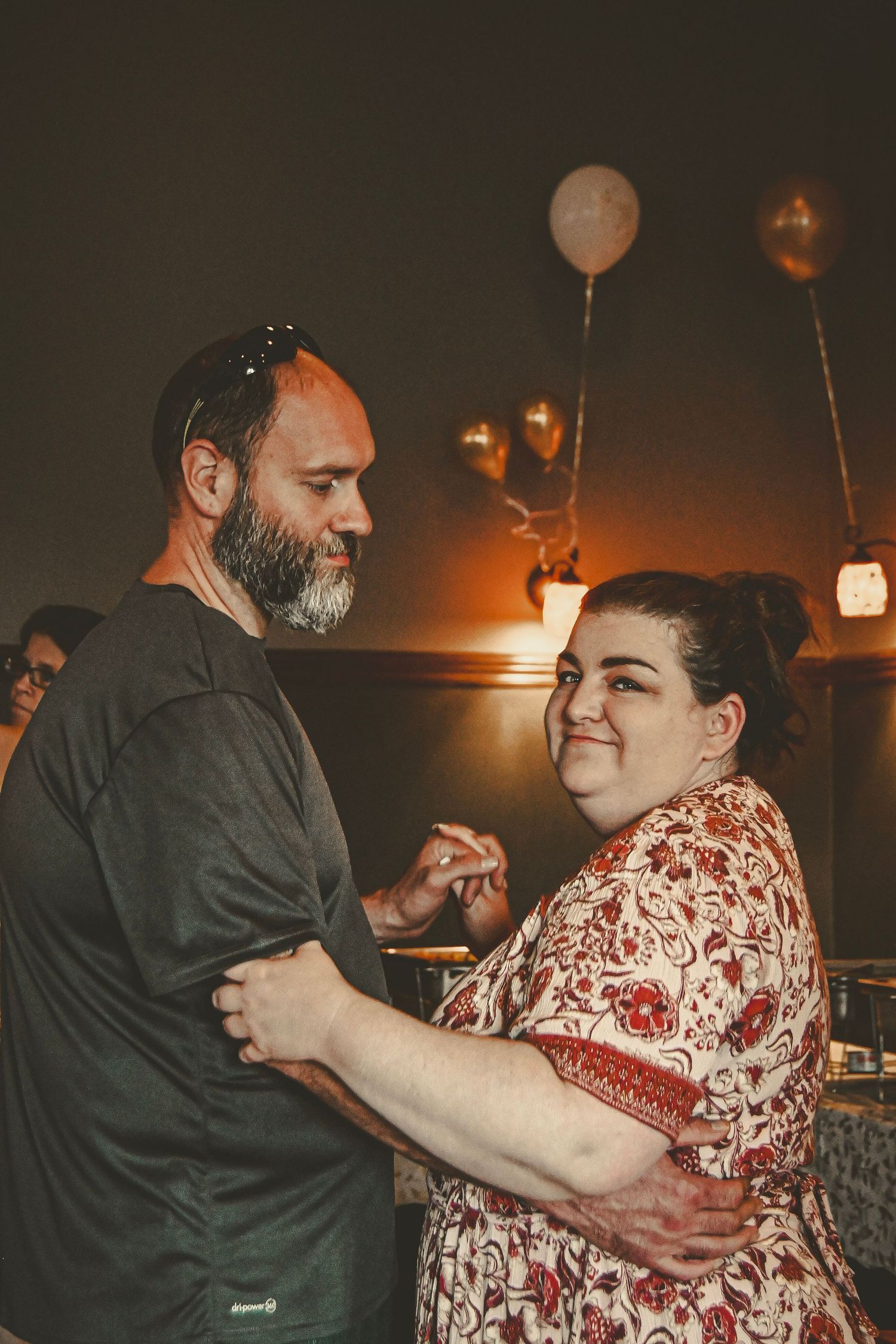 A couple sharing an intimate dance moment at an indoor event with ambient lighting and balloons.