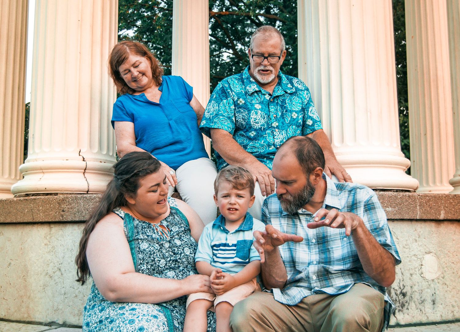 Family group sitting and laughing together on outdoor stone steps with white columns.