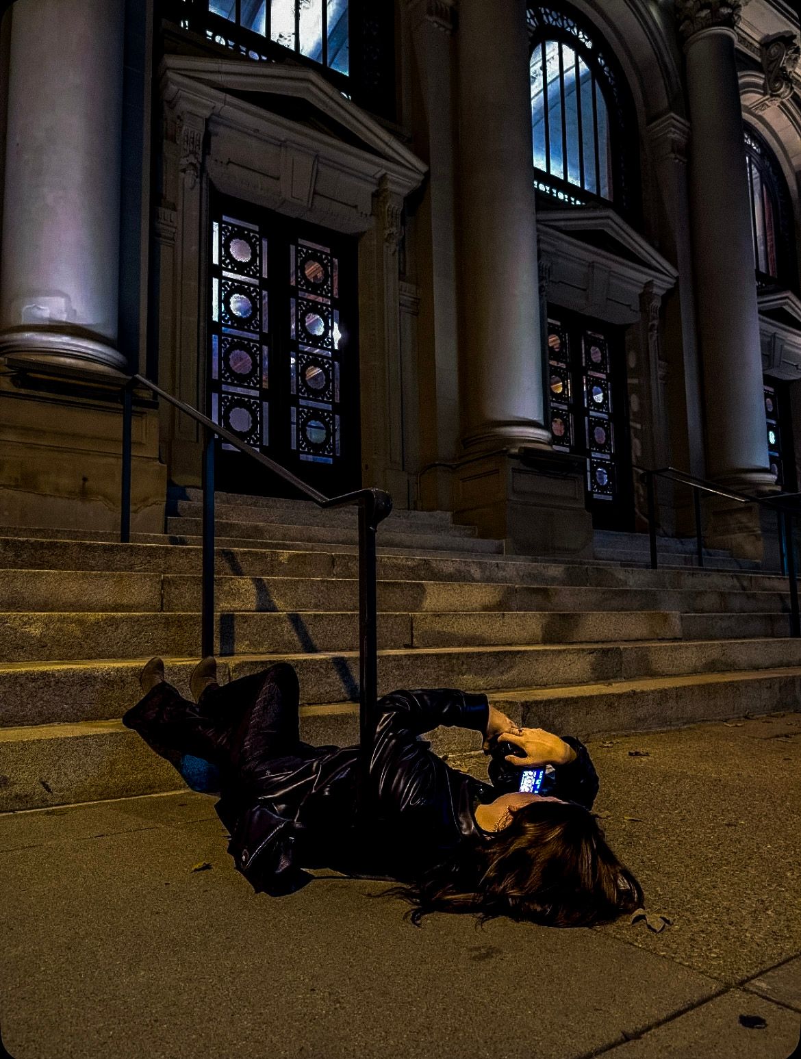 Person in black clothing lying on stone steps at night near ornate windows.