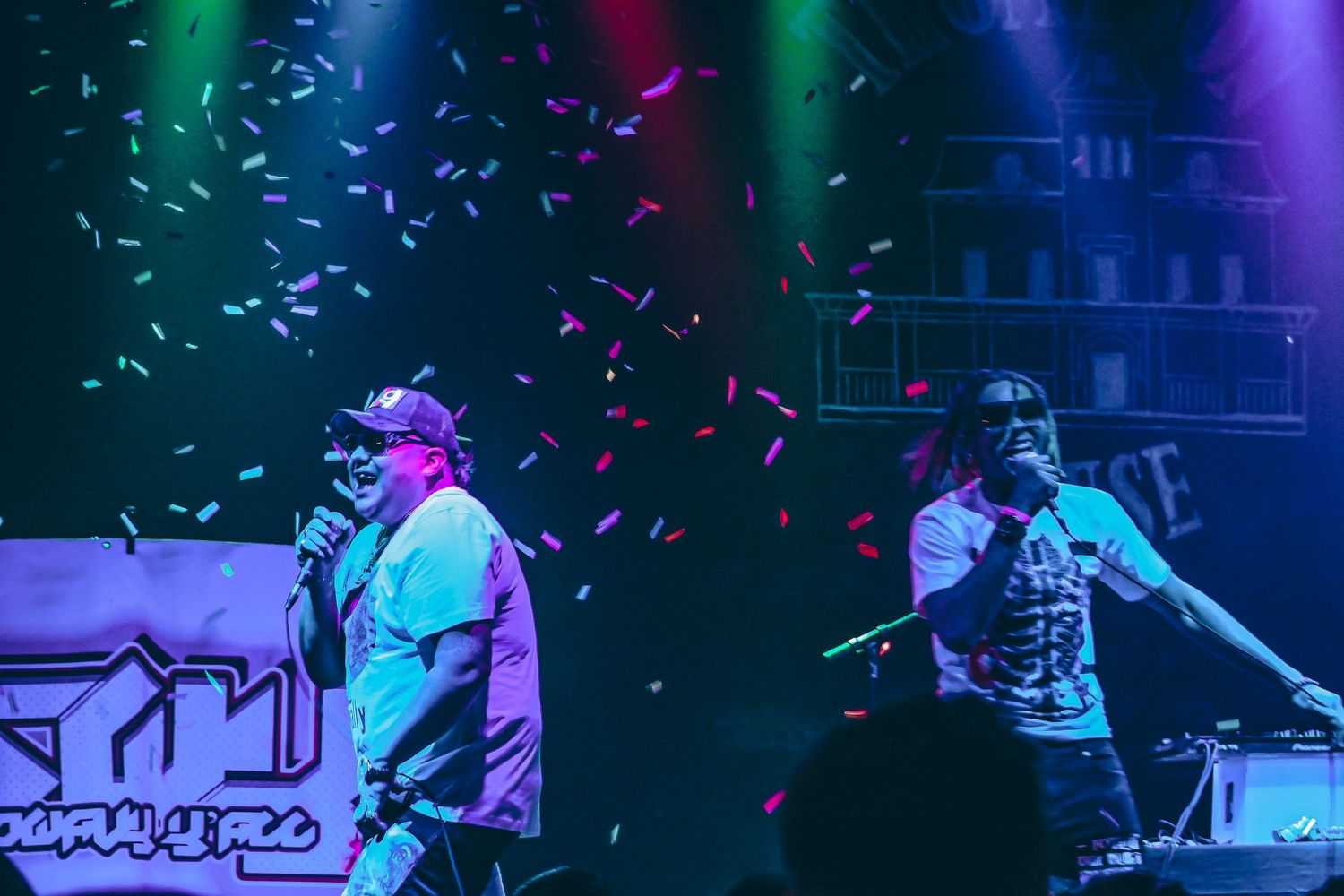 Colorful confetti falls under vibrant stage lighting at a performance venue.