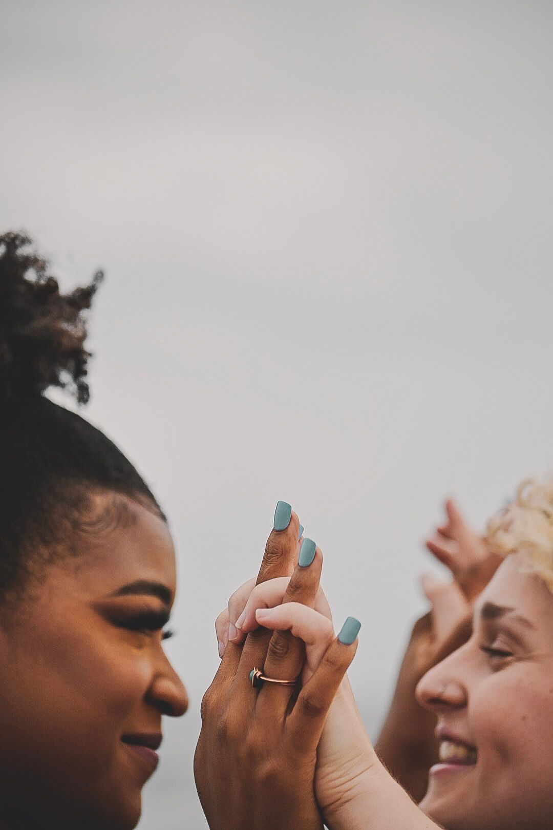 Two people share a joyful moment while holding up their hands in a playful interaction against a light background.