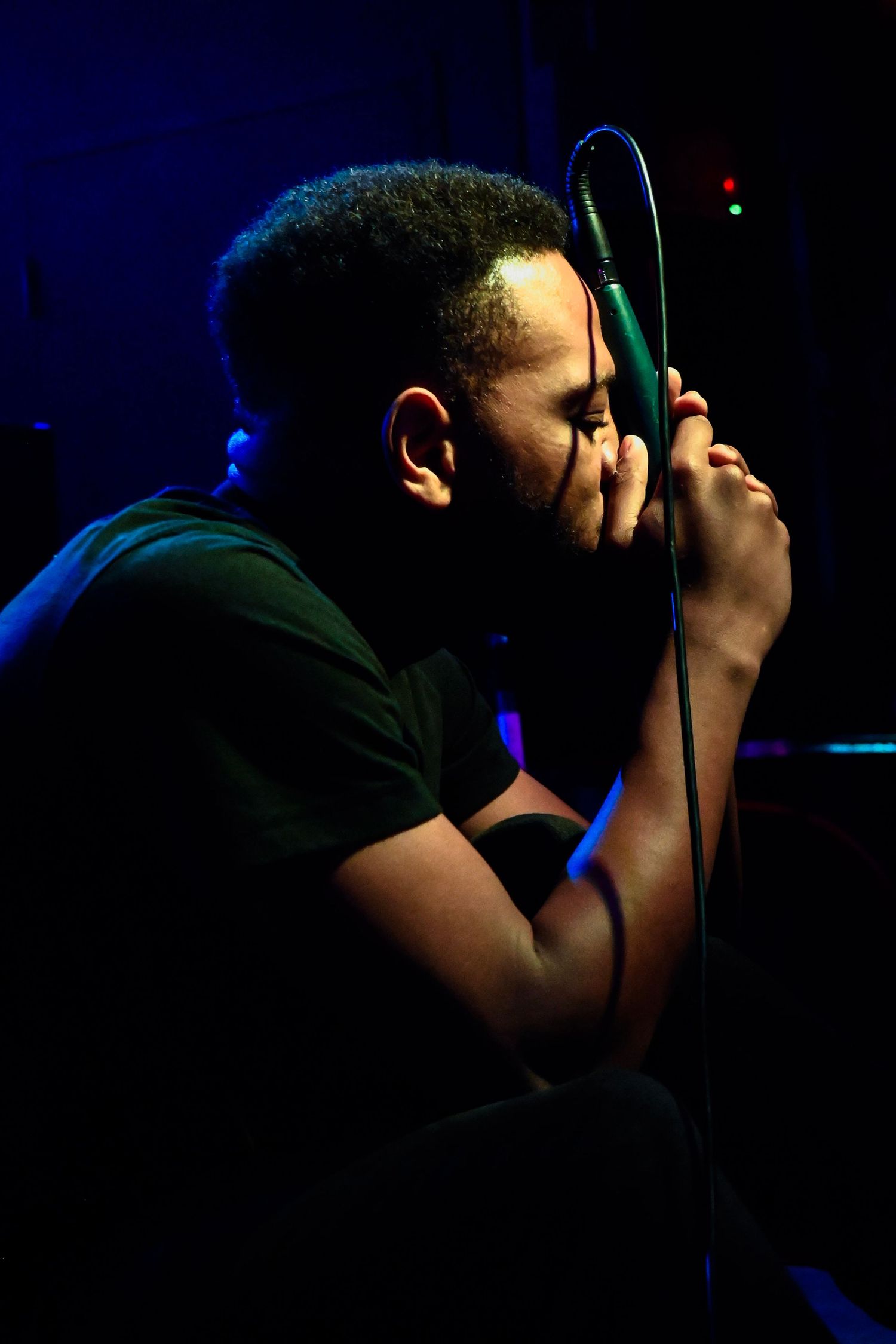Silhouette of a performer singing into a microphone in dramatic blue lighting.