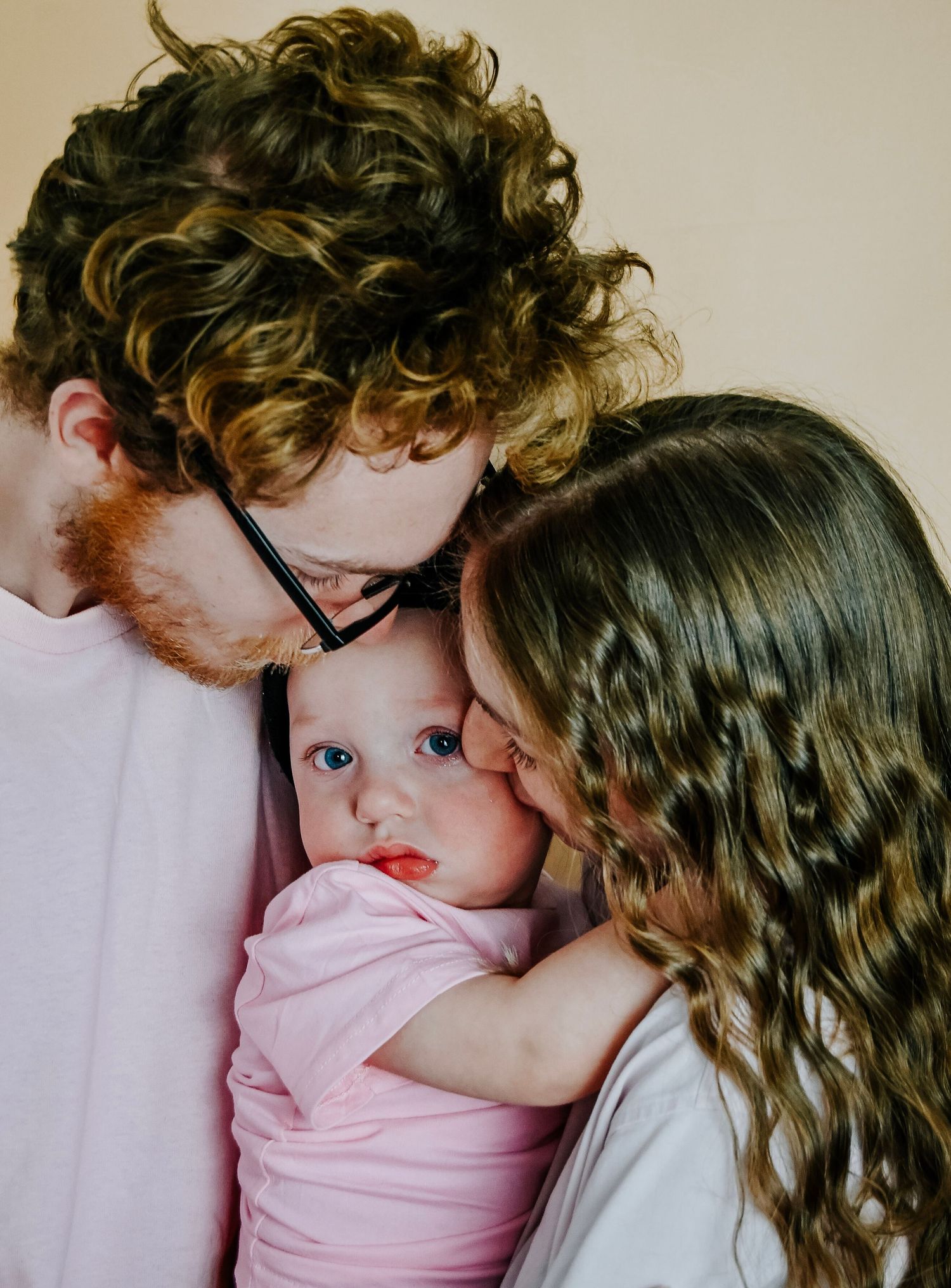 Two parents lovingly nuzzle their blue-eyed baby dressed in pink.
