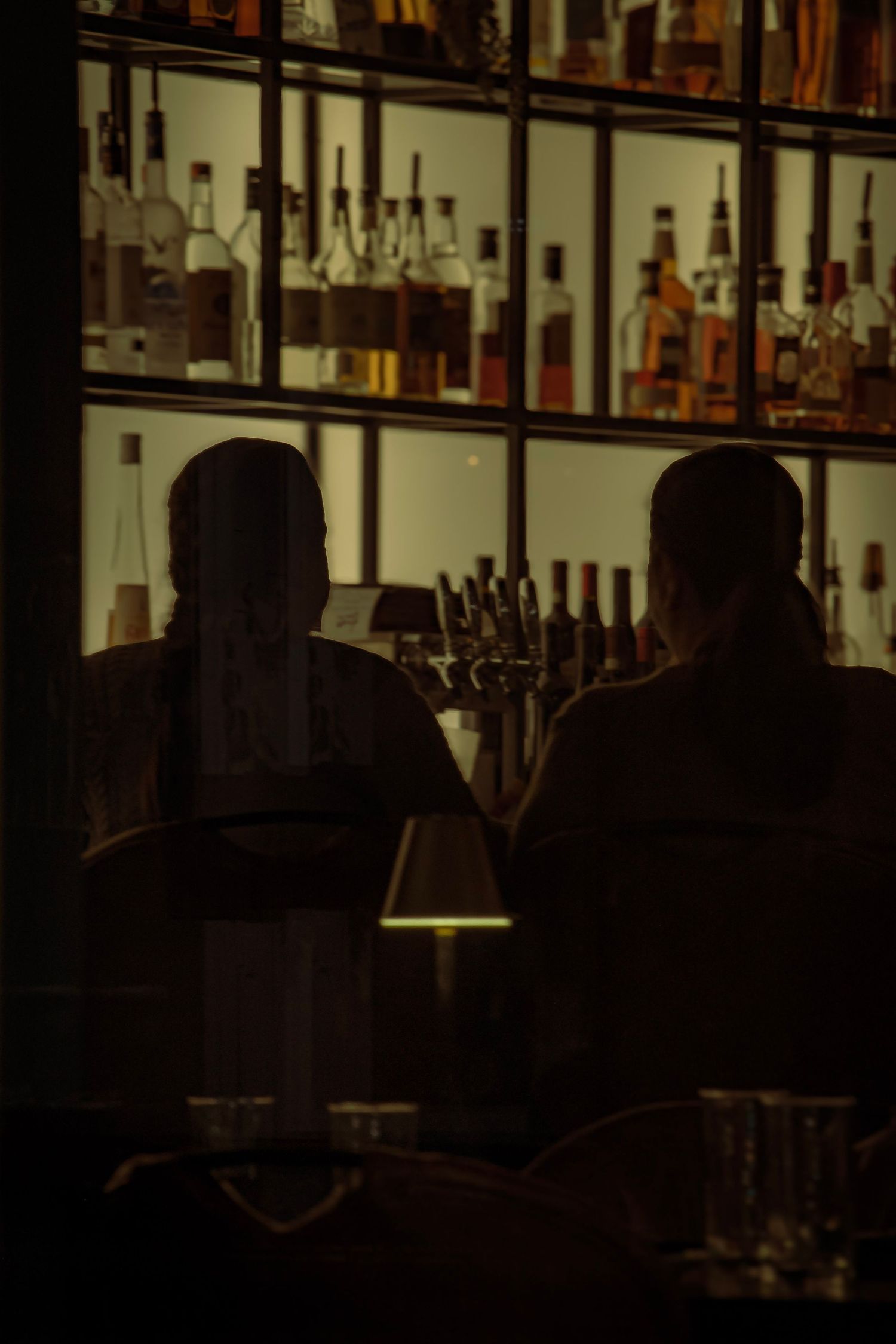 Dark moody bar interior with silhouetted bottles on shelves.