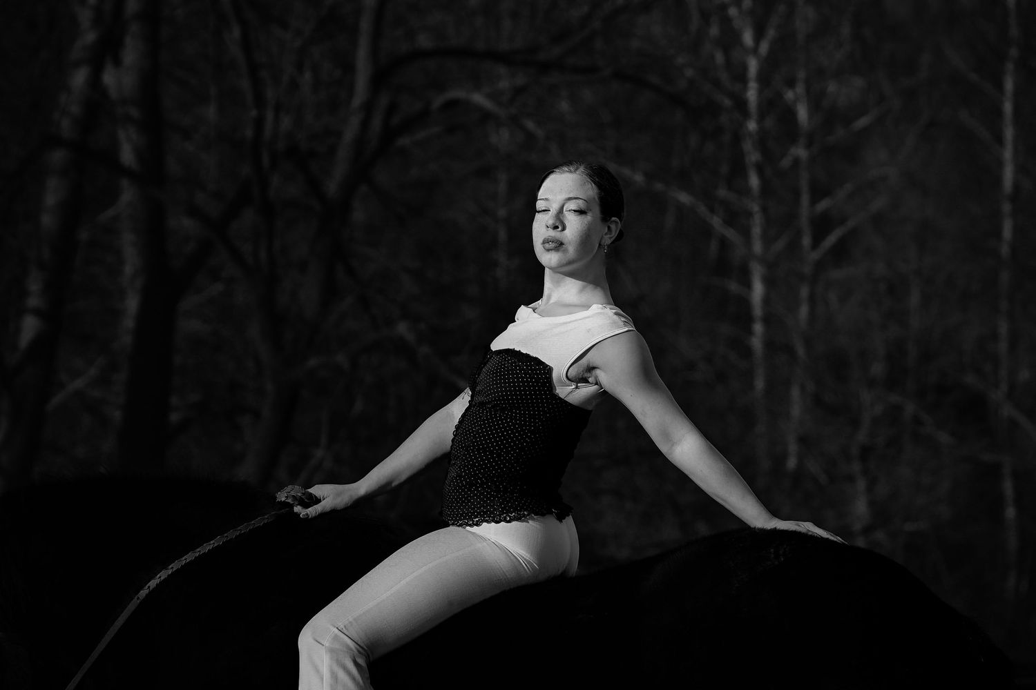 Black and white photo of a dancer in an expressive pose against a dark forest background.