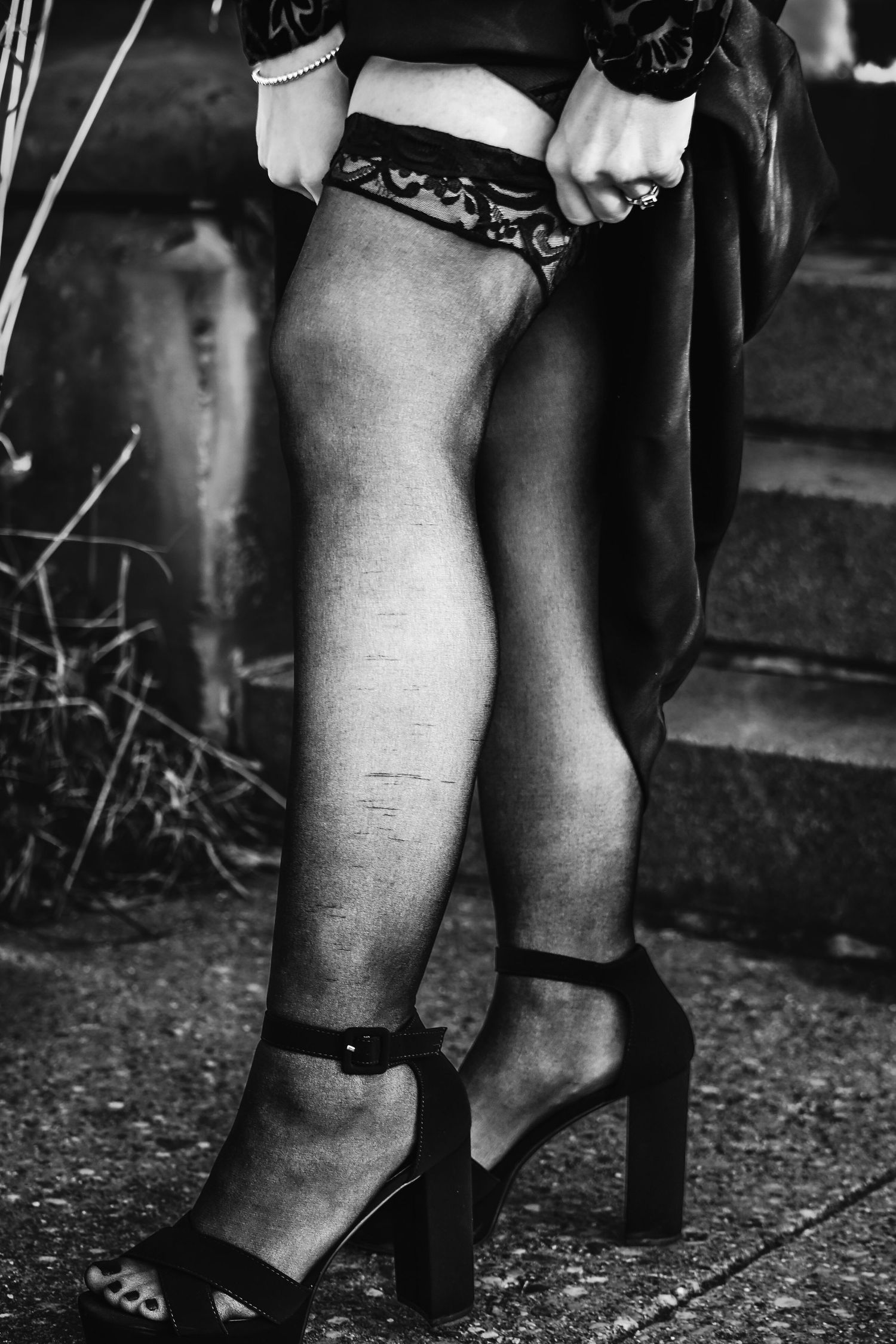 Black and white photo of legs in high heeled sandals and garter belt details against a dark background.