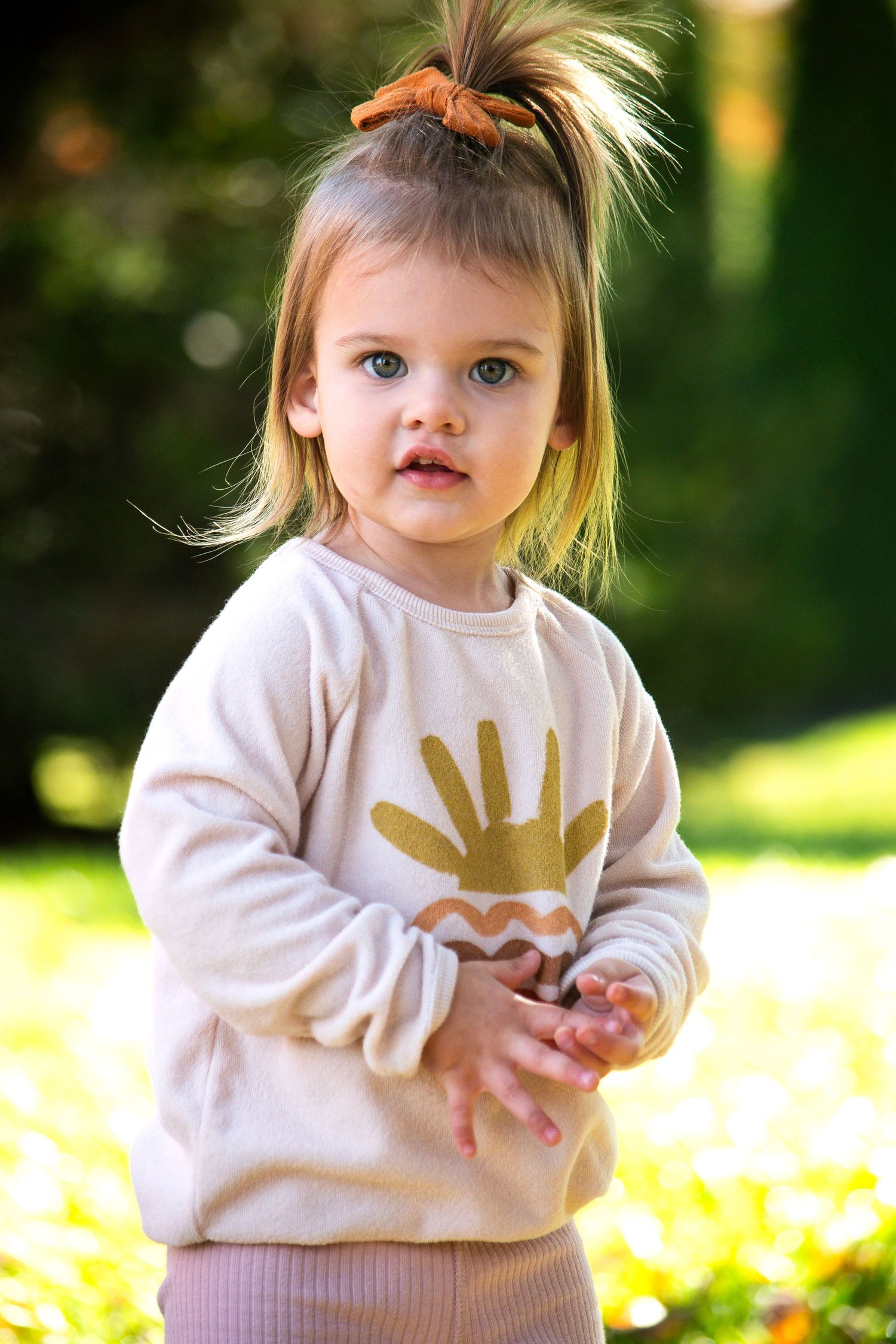Small child wearing cream sweatshirt with gold handprint design outdoors.