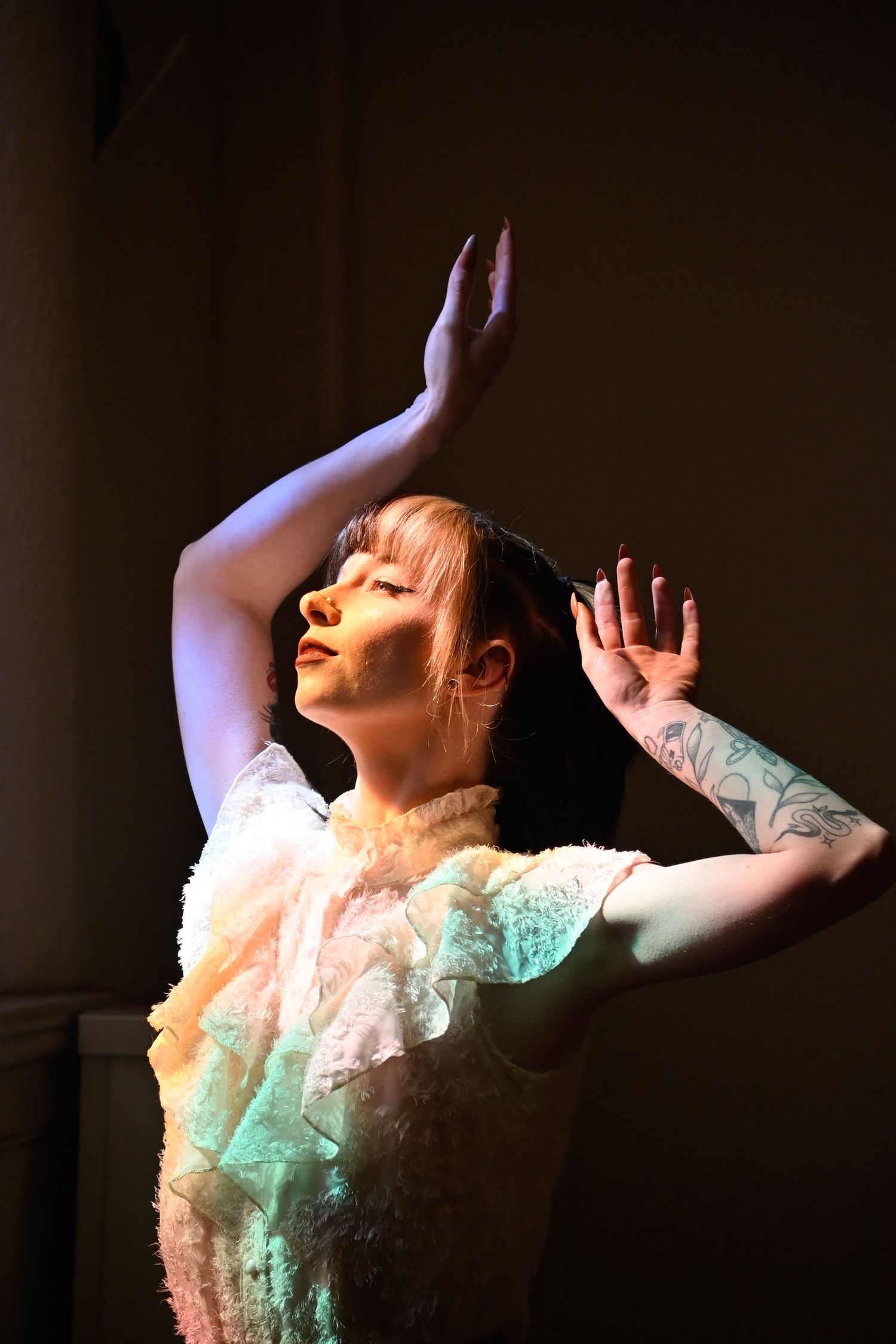 A dancer in a white lace dress performs an expressive pose with raised arms under dramatic stage lighting.