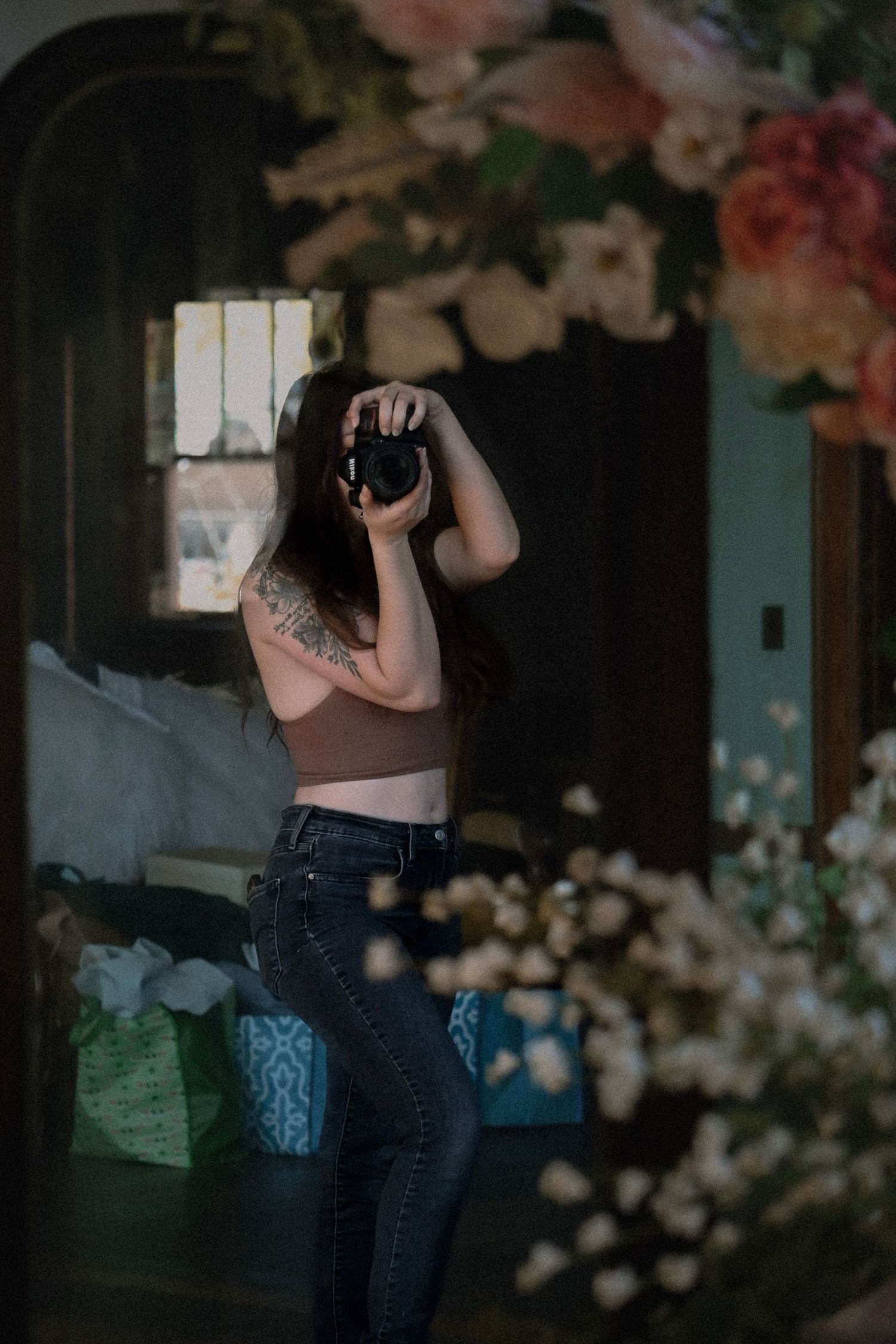 A series of dark moody photographs showing a person in jeans against floral decorations and window light.