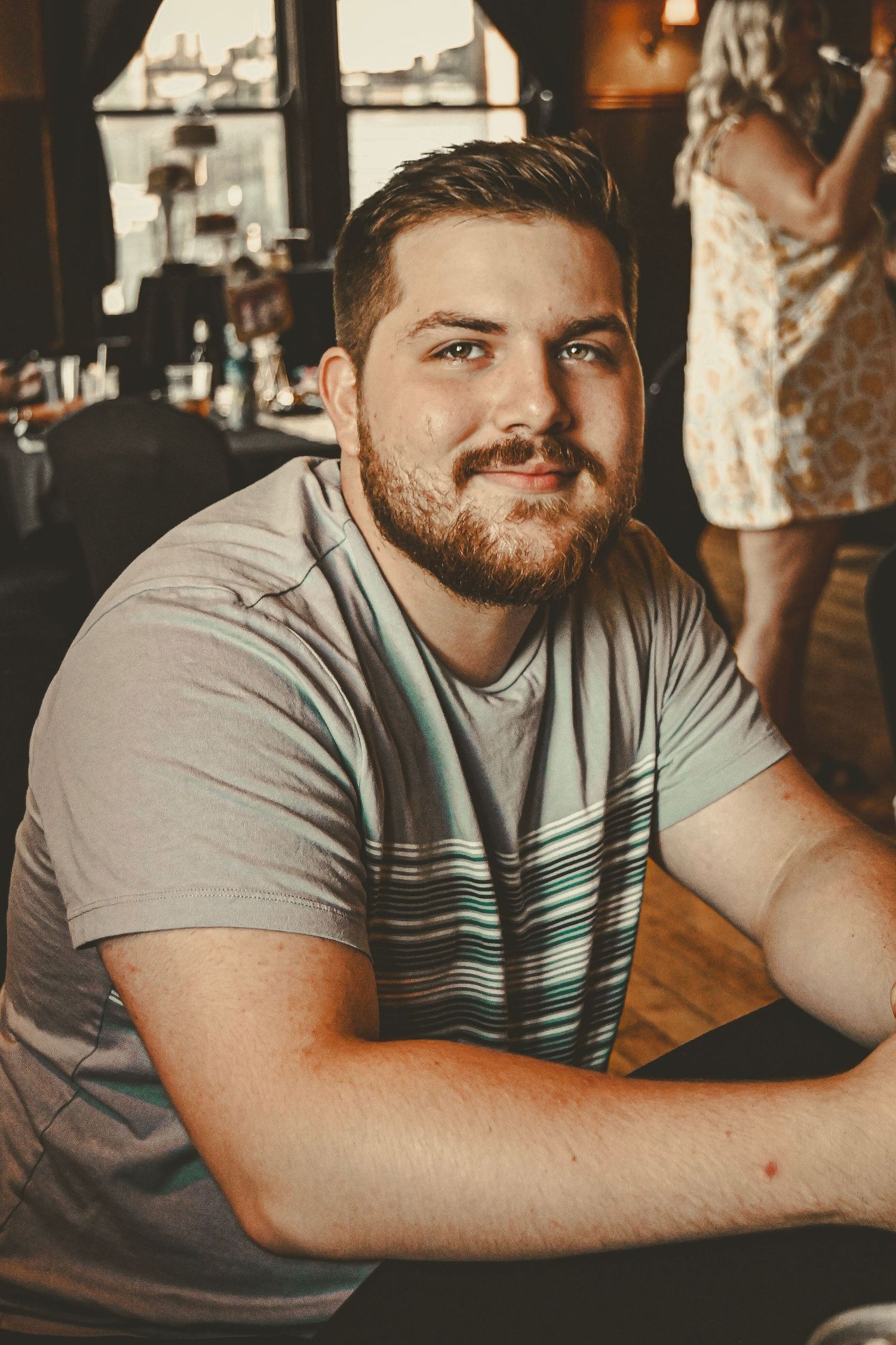 Warm-toned casual portrait of someone in a striped t-shirt at a restaurant or cafe.