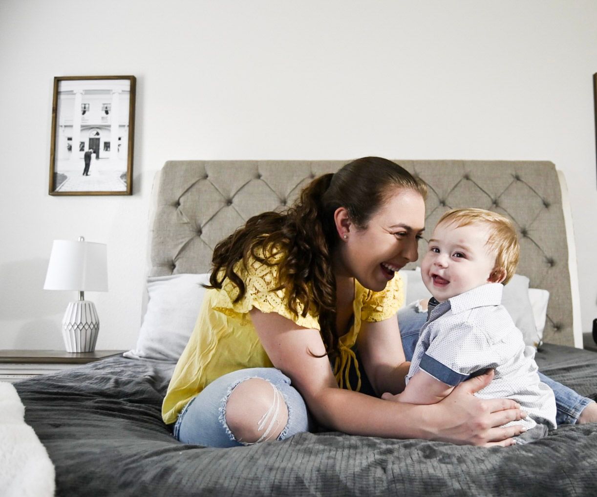 Candid family moments captured on grey bedding with tufted headboard in background.