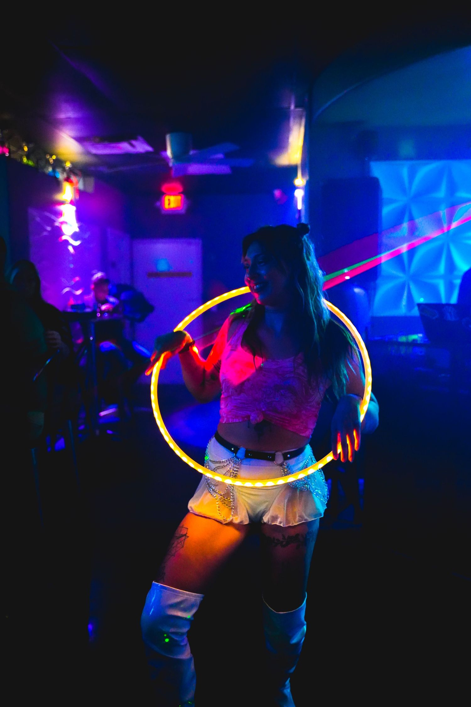 Silhouettes of performers with glowing LED hoops creating light trails in purple and blue.