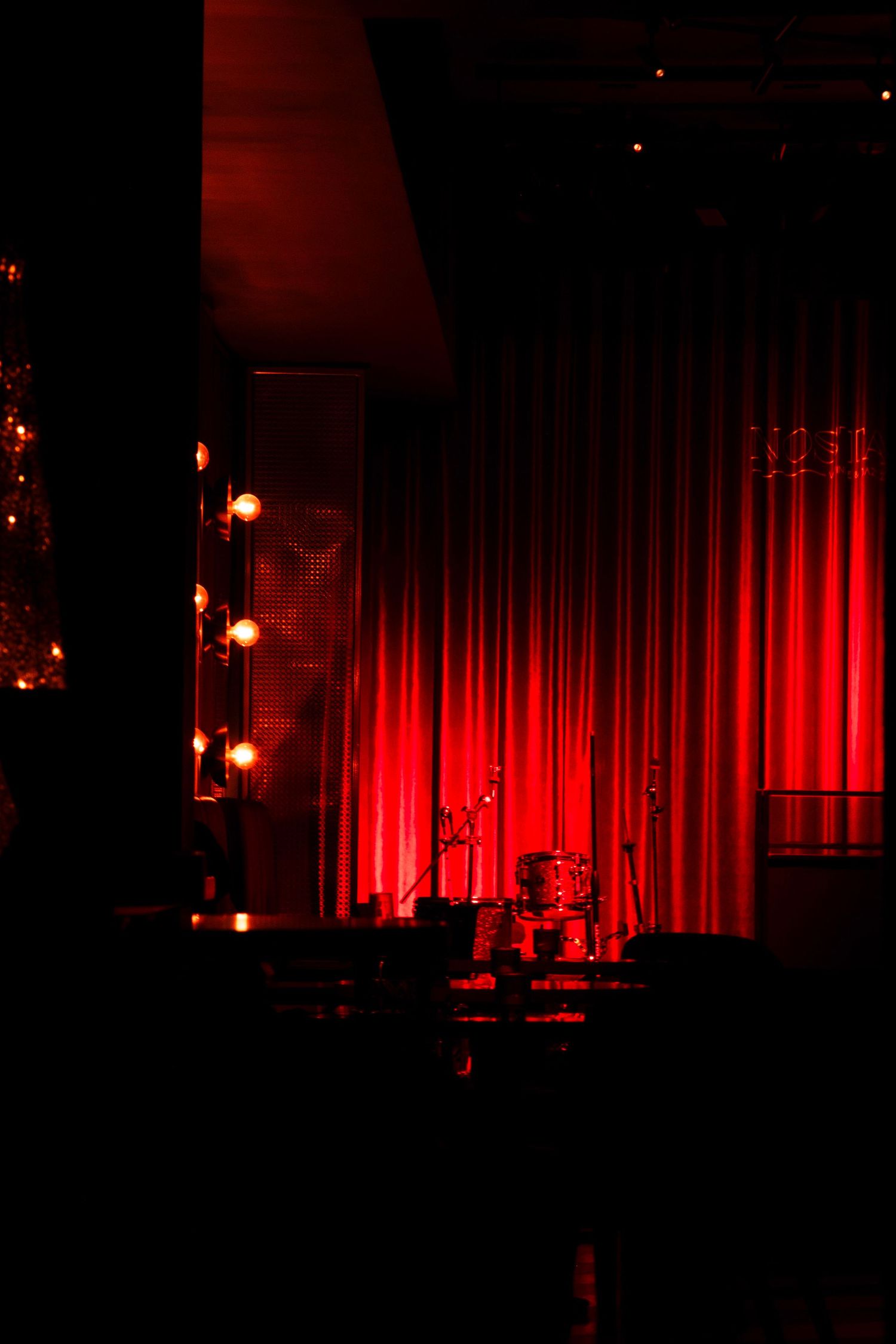 An empty stage setup with dramatic red curtains and ambient lighting.
