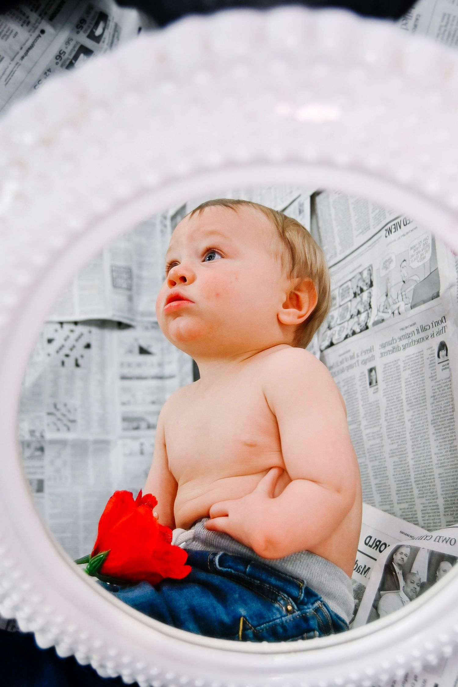A baby in denim lies on newspaper backdrop with red heart prop in artistic black and white newborn photography series.