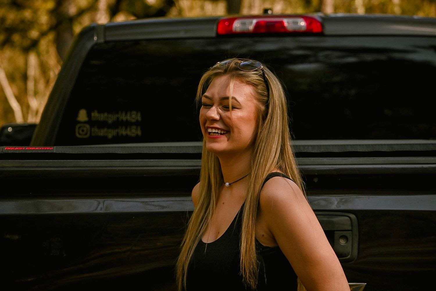 Person sitting casually on steps with black truck in background during sunset.