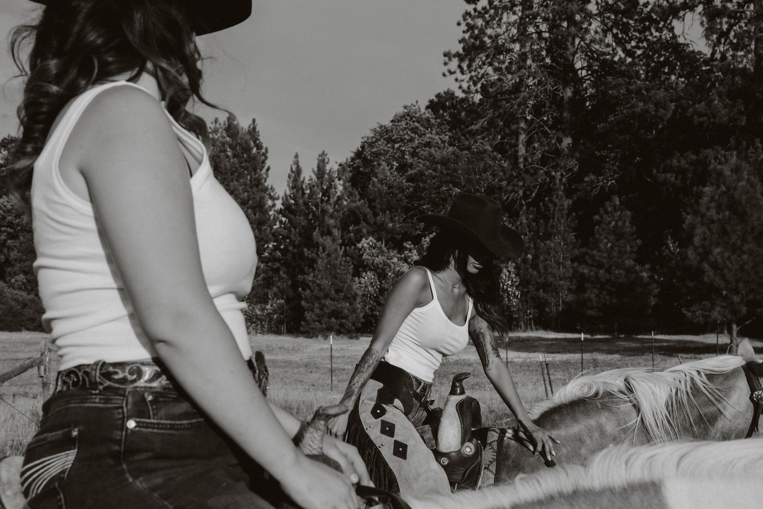 Western-style riders prepare their horses in black and white countryside scene.