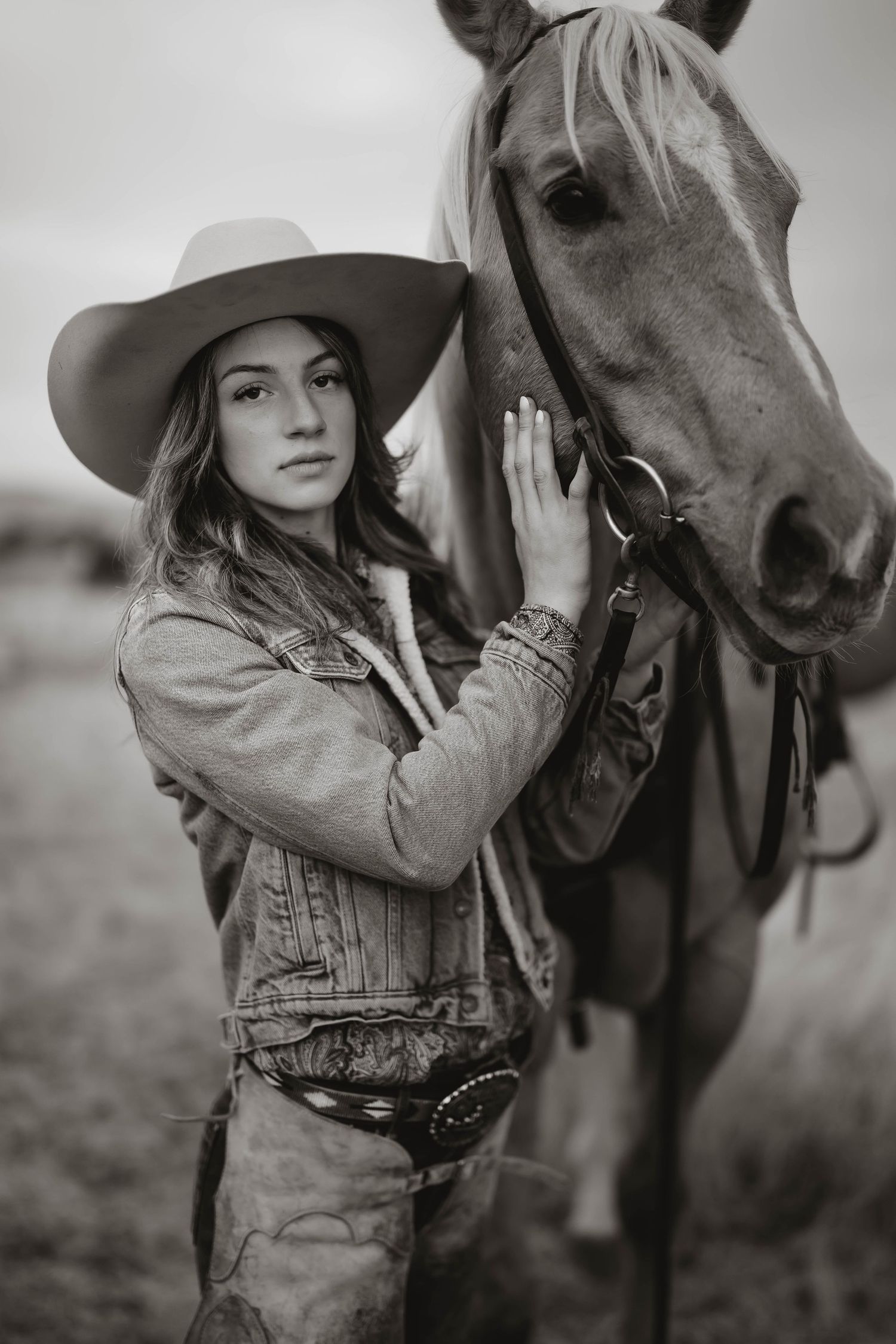 A black and white portrait of someone in western wear with a horse.