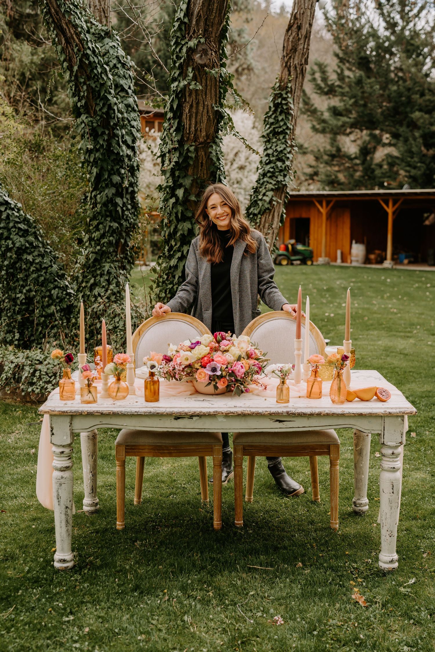 Rustic outdoor table setting with pink floral arrangements and glowing candles in a garden setting.