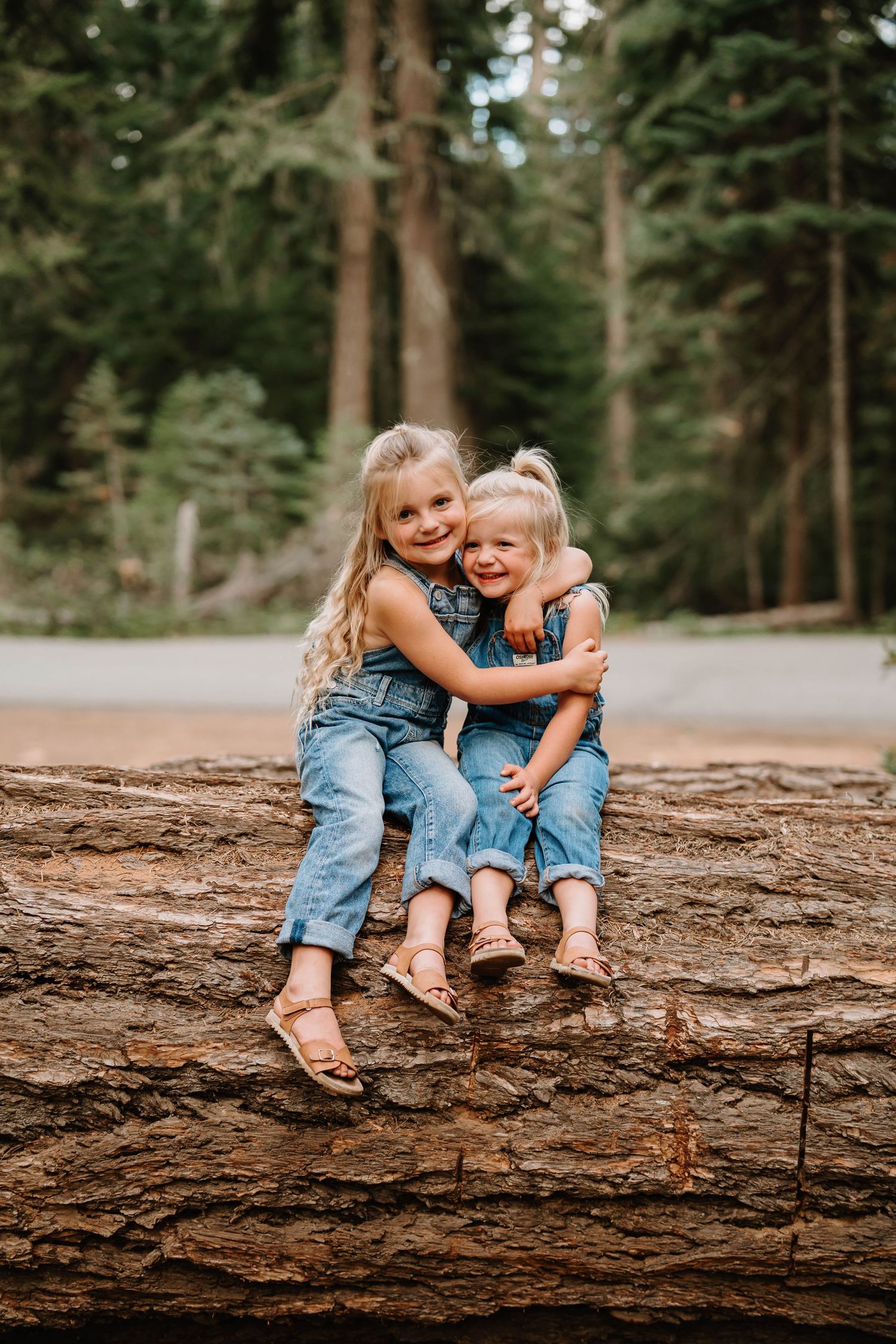 Two people in denim sitting and laughing together on a large fallen tree trunk.