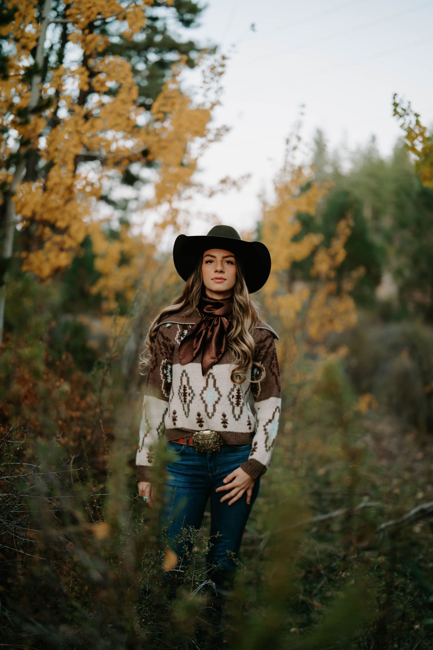 Western-styled portrait in a cowboy hat against autumn foliage background.