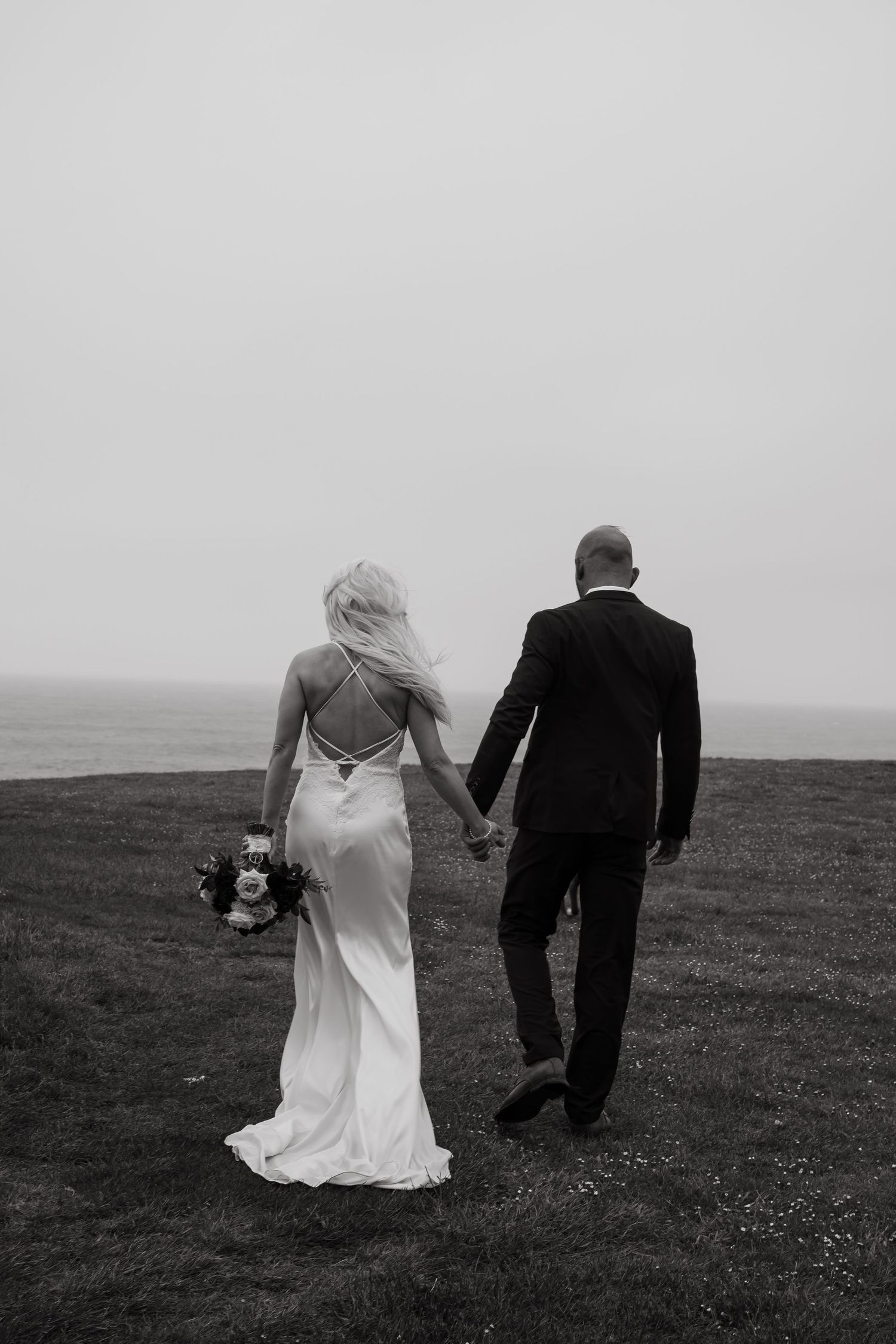 Black and white photo of newlyweds walking across a misty field.