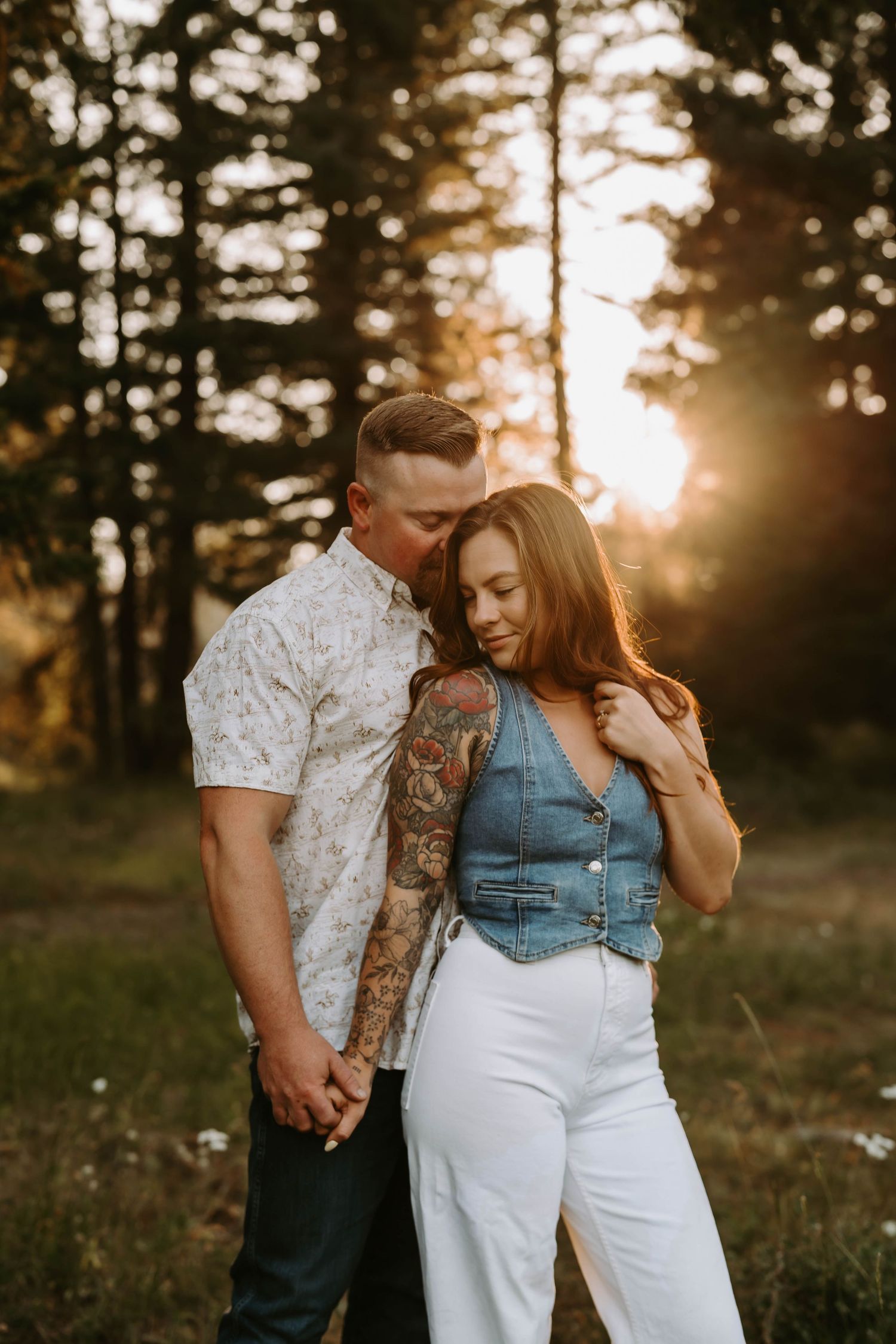 Couple sharing tender moment in sunlit field with golden sunset through trees.