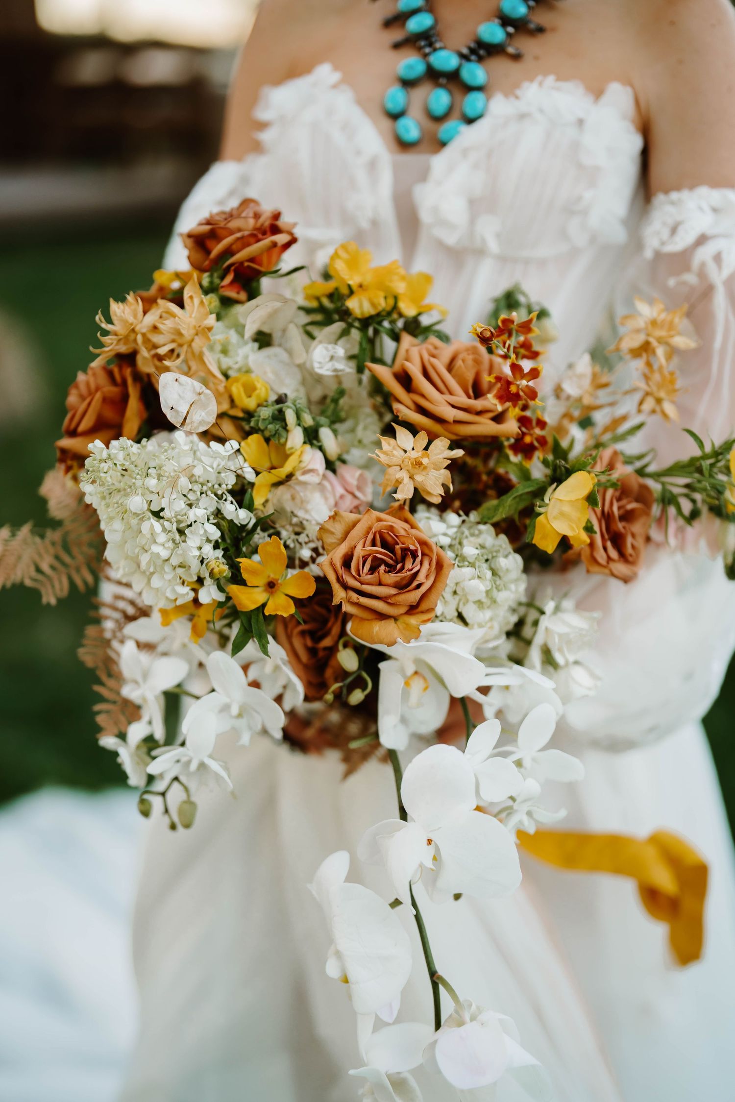 Wedding bouquet featuring white orchids, yellow daisies, and copper roses with turquoise jewelry accent.