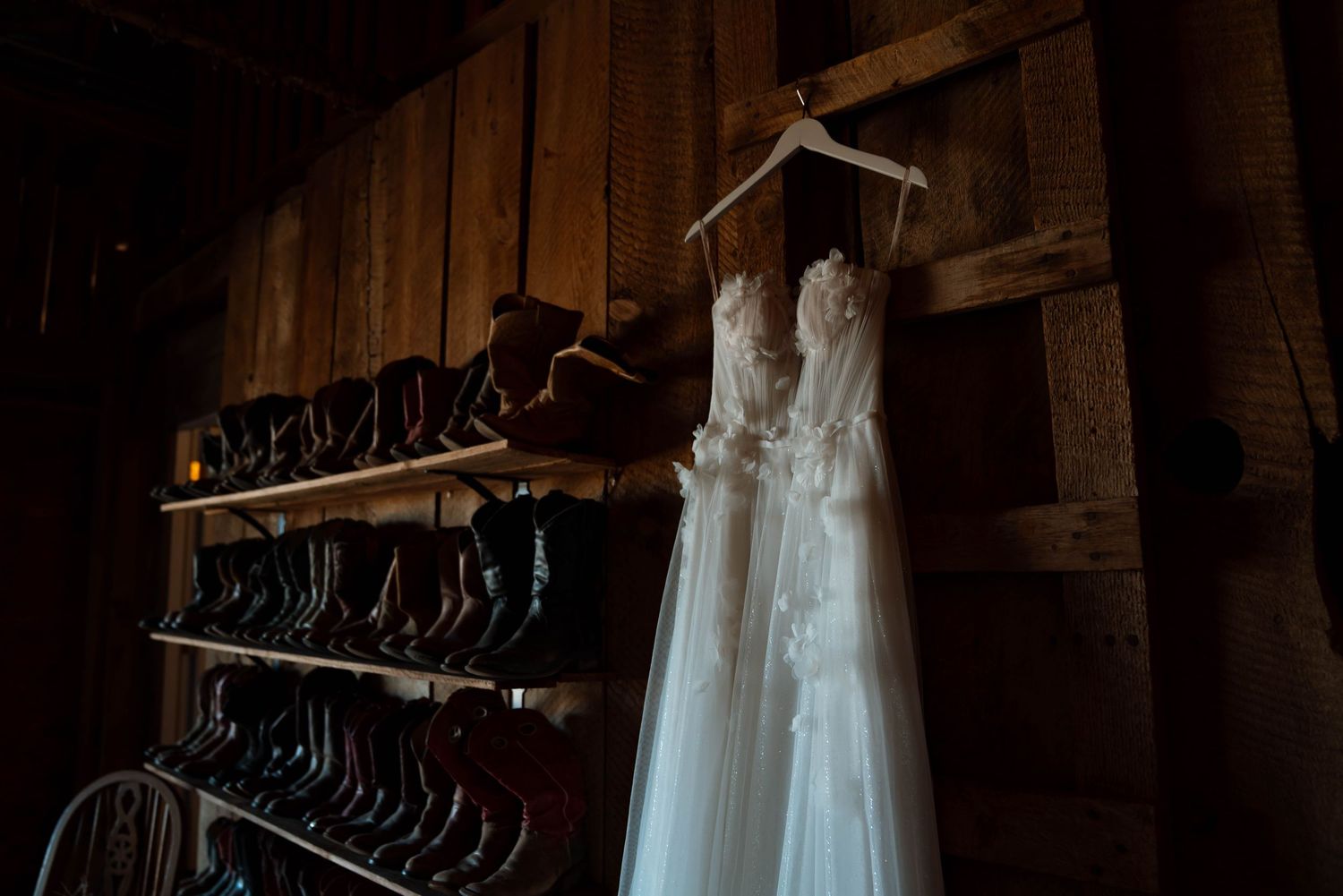 Wedding dresses hanging on wooden racks in a dimly lit rustic room.
