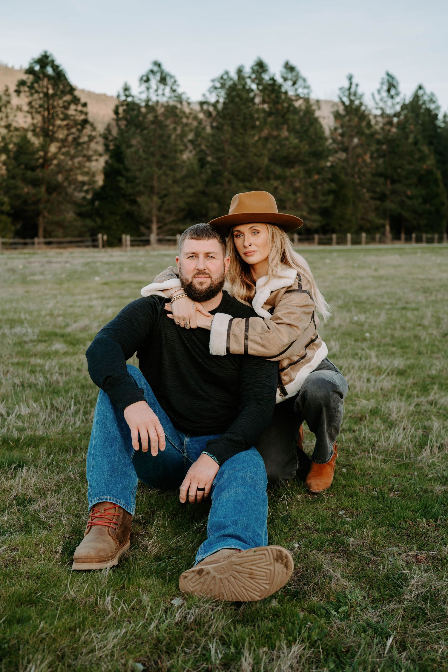 Casual outdoor couple photography session in a grassy field with pine trees.