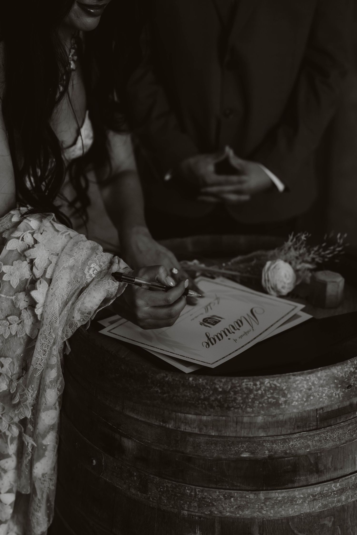Black and white close-up of hands signing a wedding document.