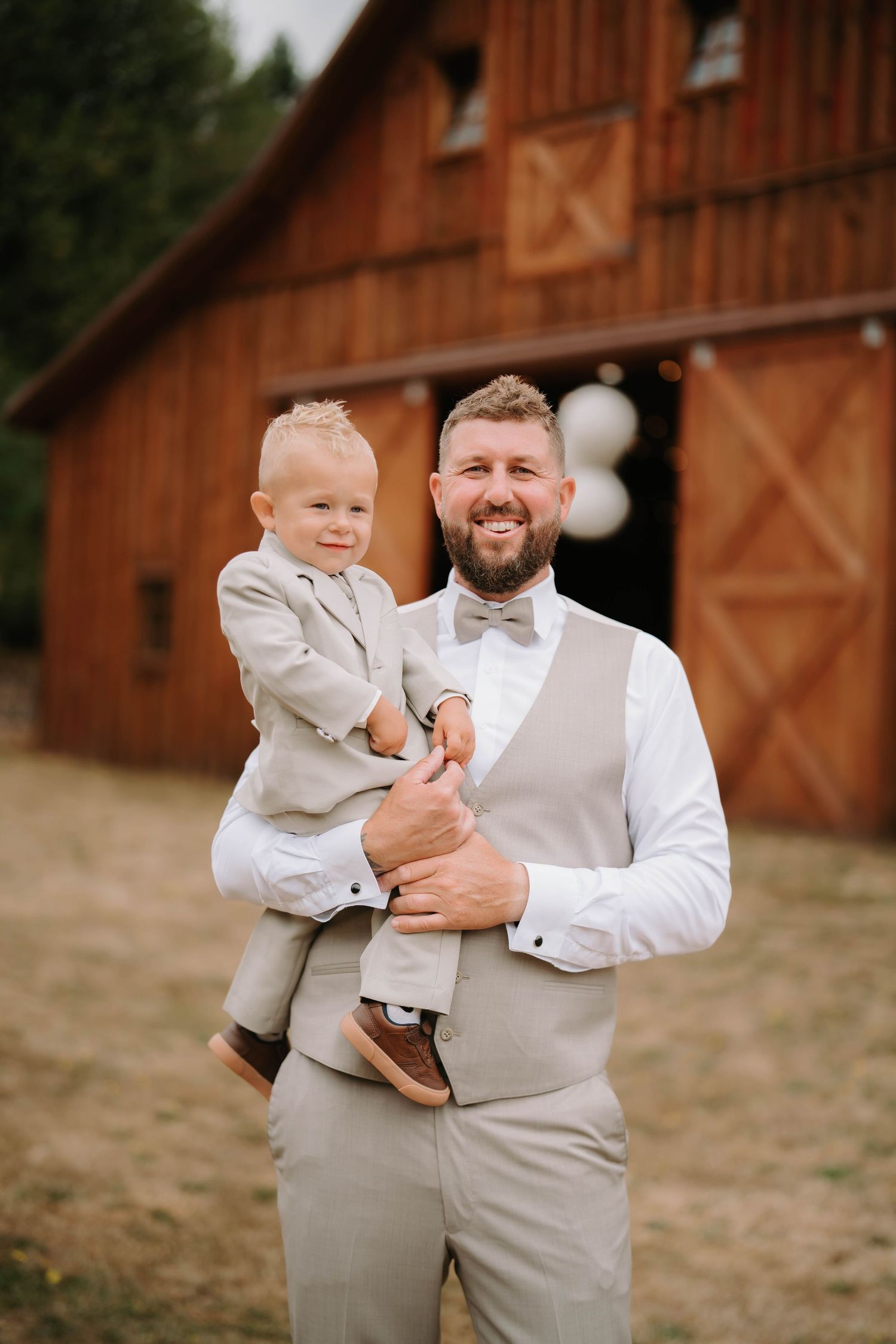 Sweet moments between a father and young child in matching formal wear by a rustic barn.