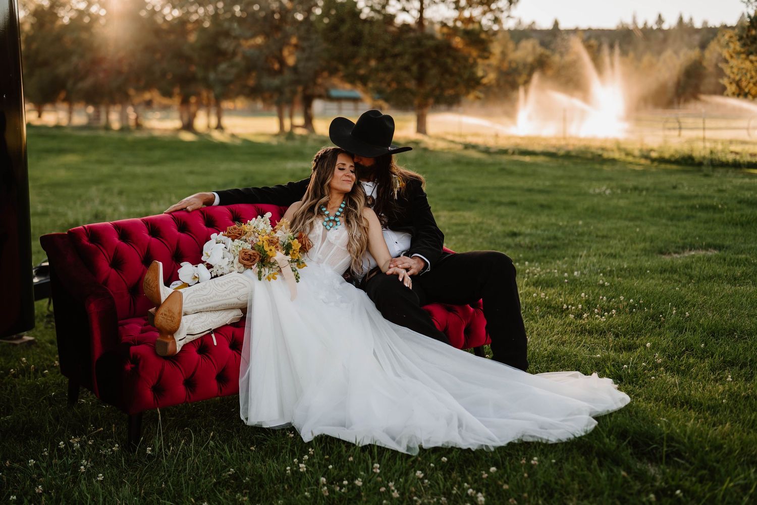 A red velvet couch sits in a grassy field during golden hour.