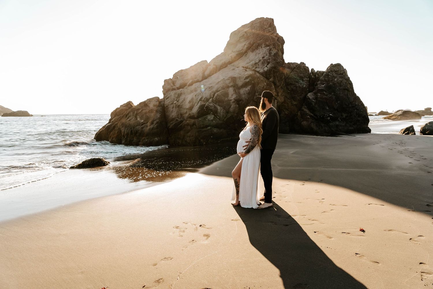 Couple walking along dramatic black sand beach with coastal rock formations.