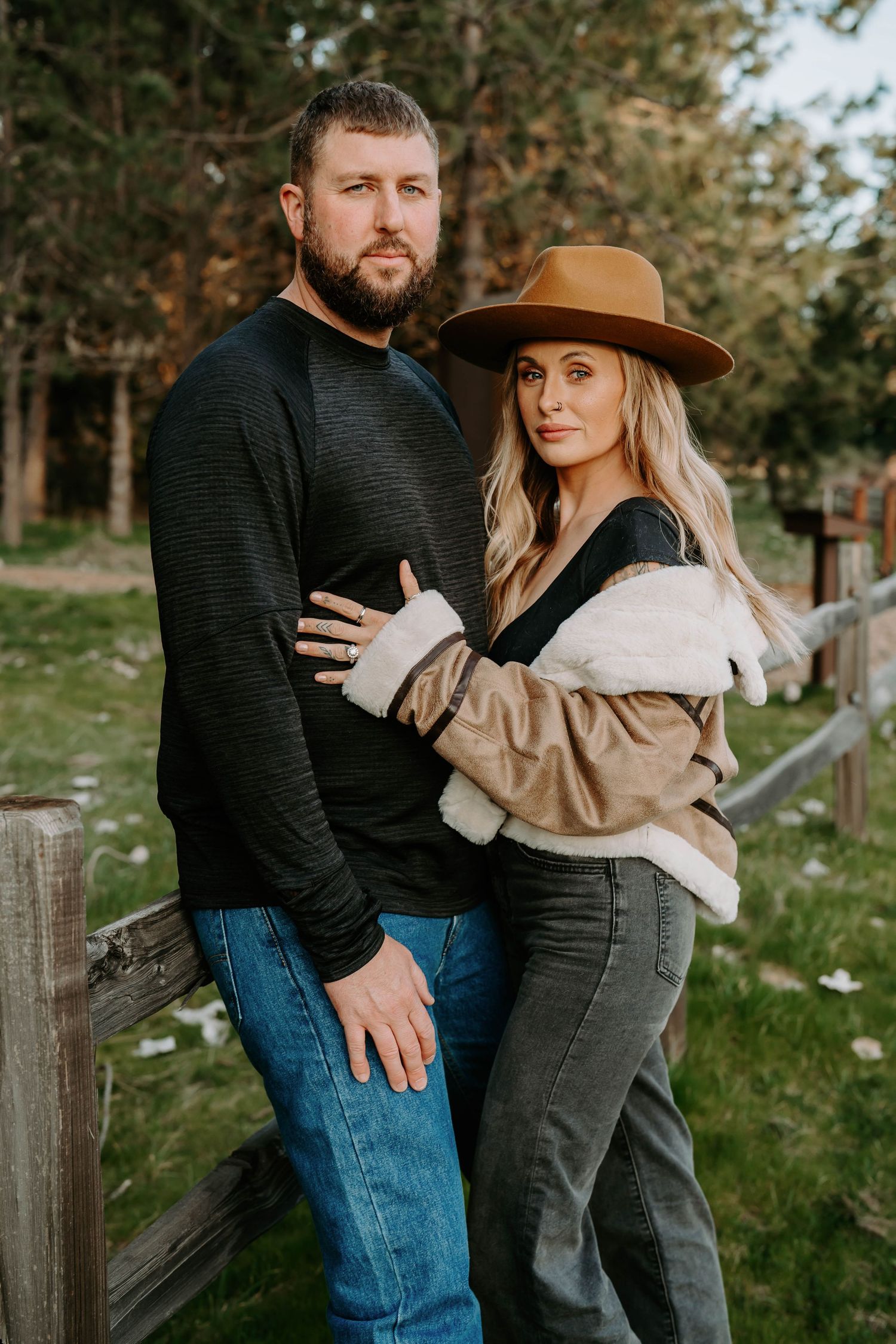 A romantic outdoor photoshoot featuring a couple leaning against a wooden fence.