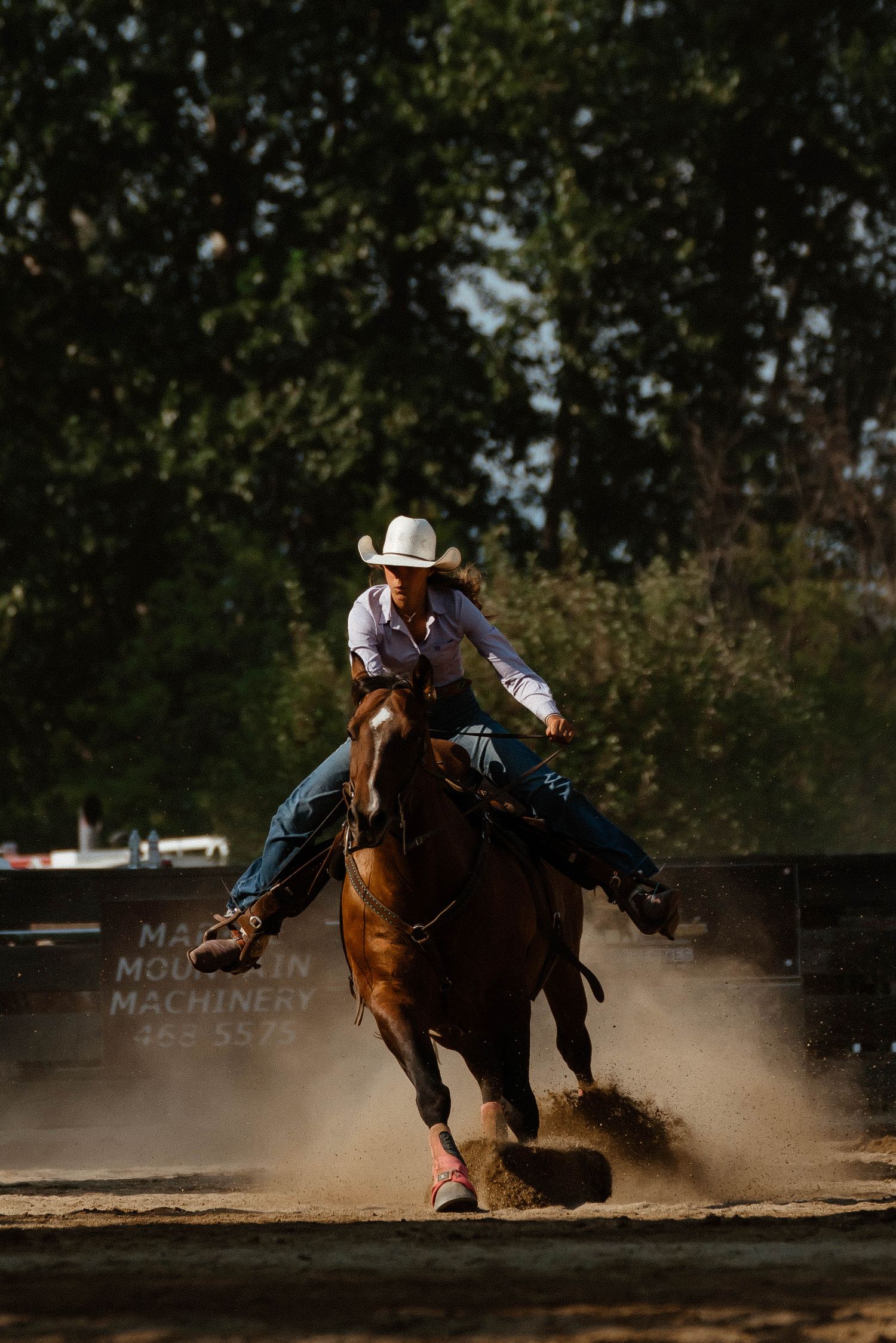 A rodeo rider performs a dramatic barrel racing turn kicking up dust in the arena.