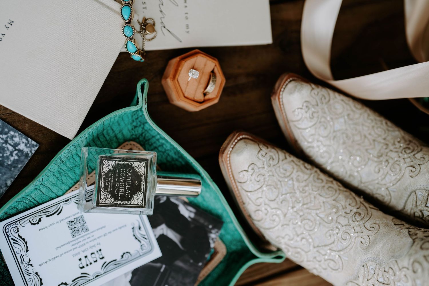 Close-up details of wedding day preparations including rings, invitations, and turquoise accents on a rustic wooden surface.