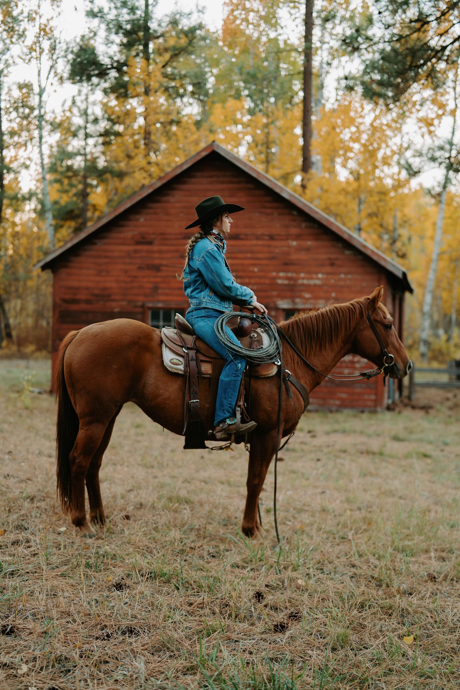 Rider in turquoise western wear on horseback near rustic red cabins in autumn.
