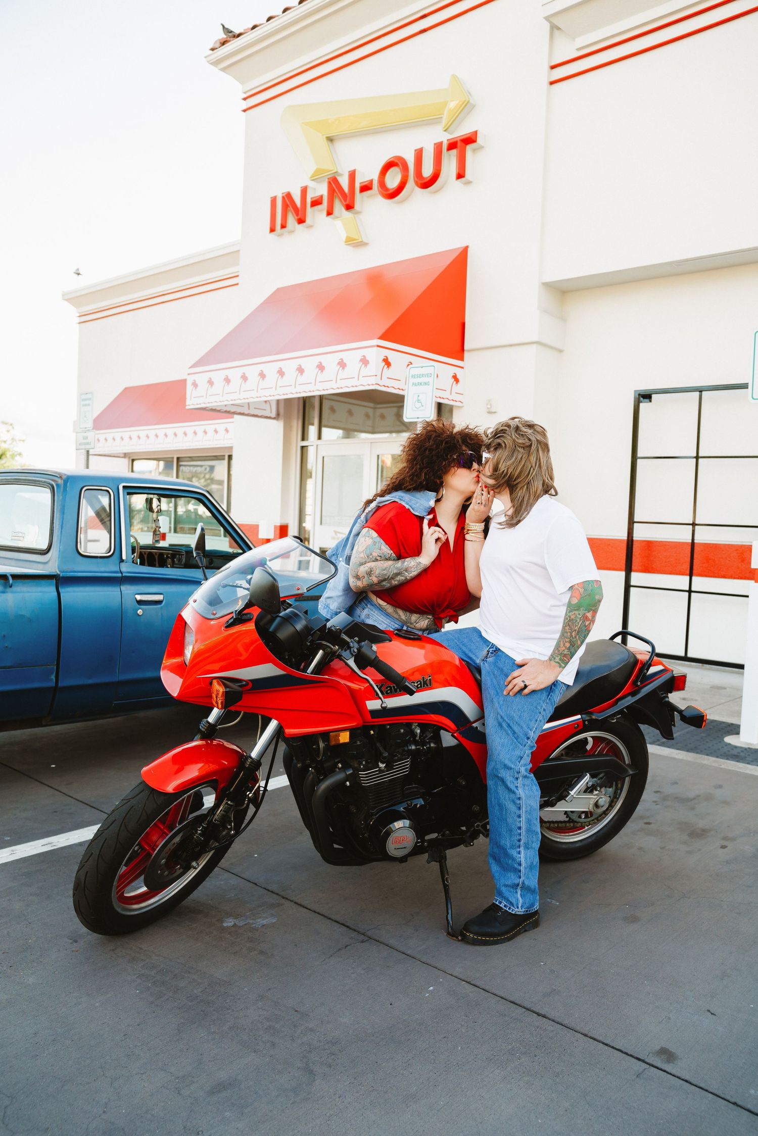 Red motorcycle parked outside In-N-Out burger restaurant with denim-clad rider checking the bike.