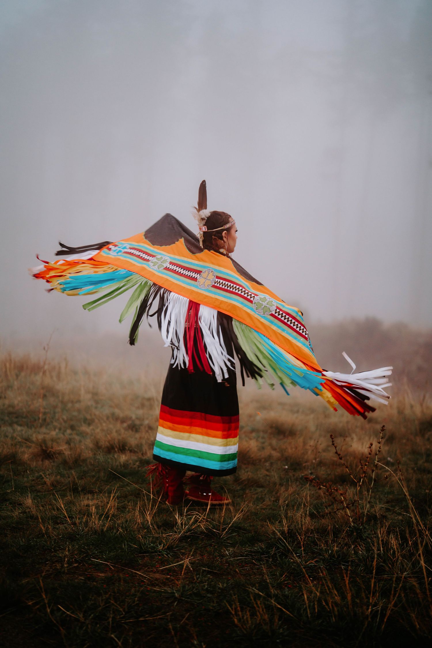 Person wearing vibrant indigenous regalia spins in a misty field creating a colorful motion effect.