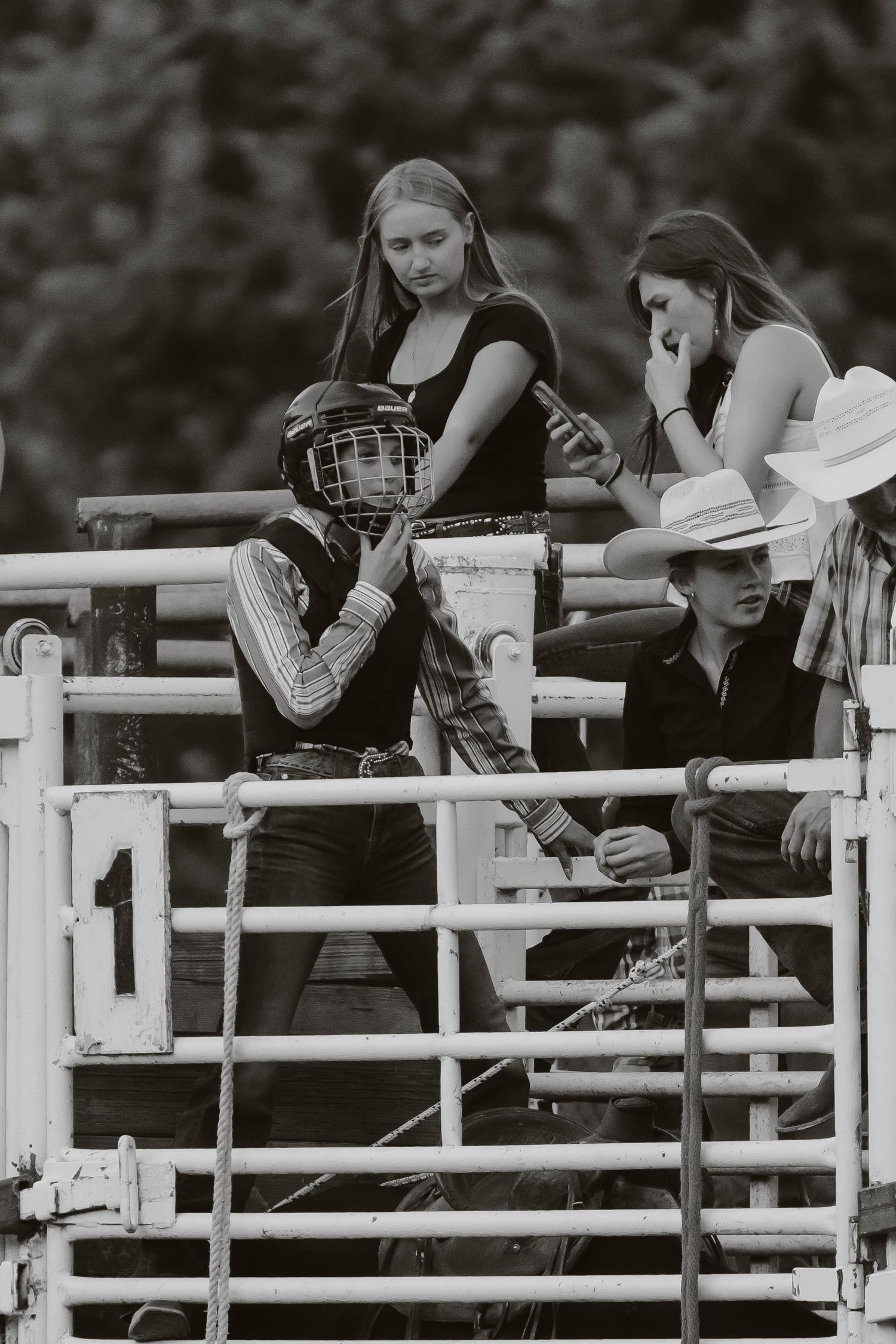 Spectators lean on white fence railings watching a rodeo event.