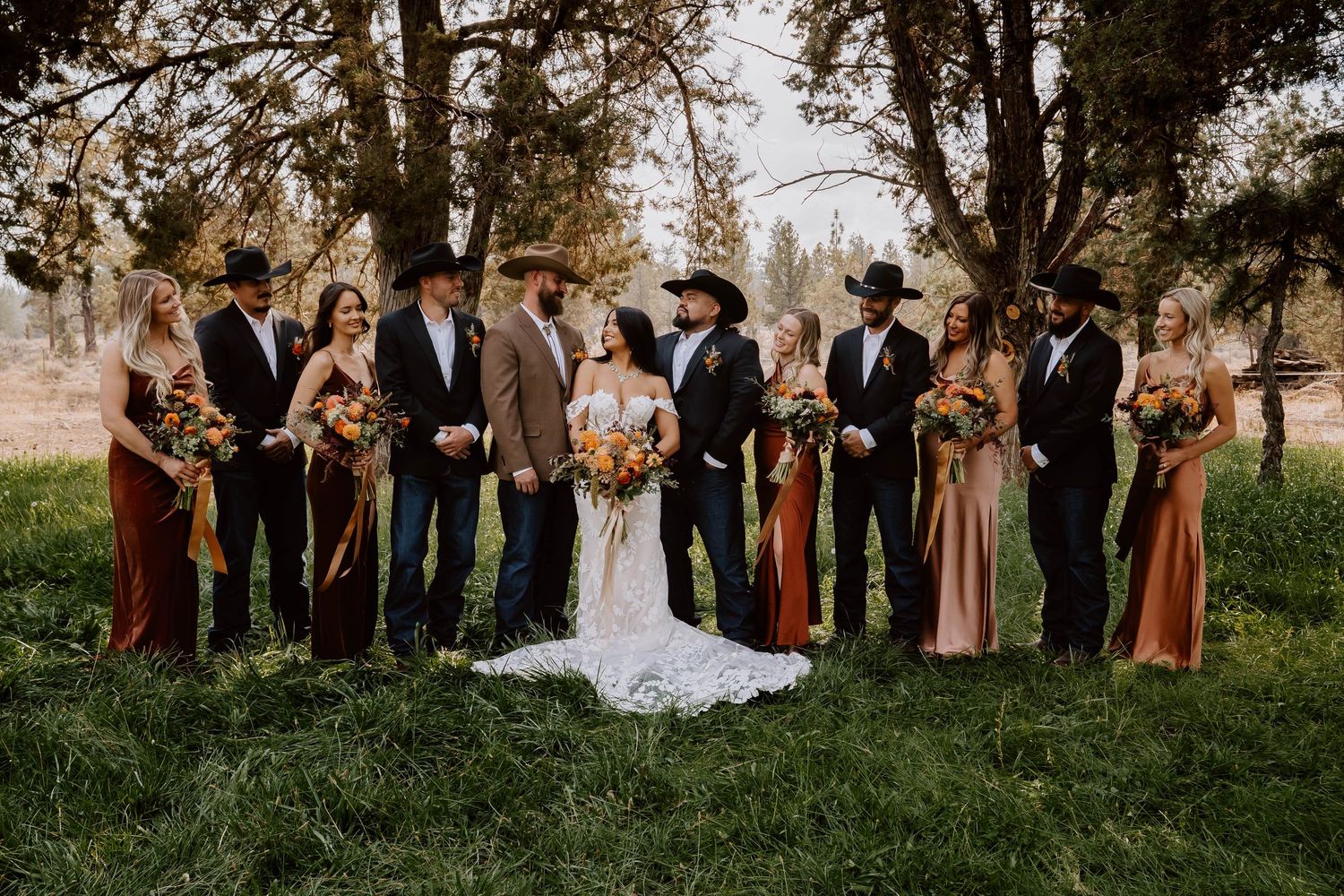 Wedding party in earth tones posed together outdoors under autumn trees.