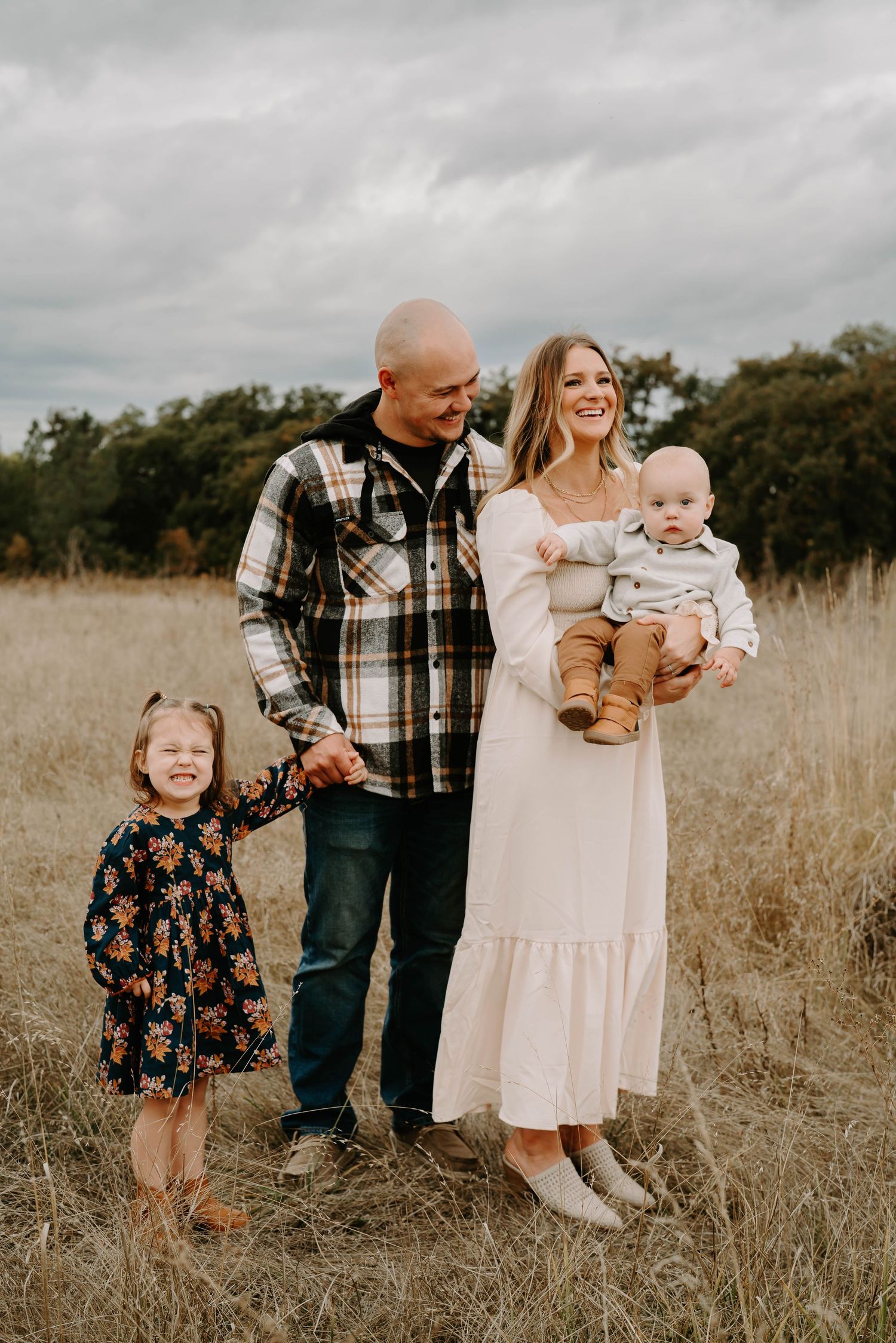 Family portrait session in a golden field with parents and young children in casual attire.
